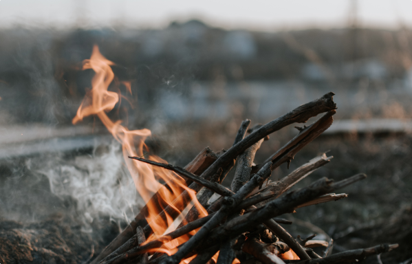 A small campfire with burning sticks and visible flames and smoke outdoors.