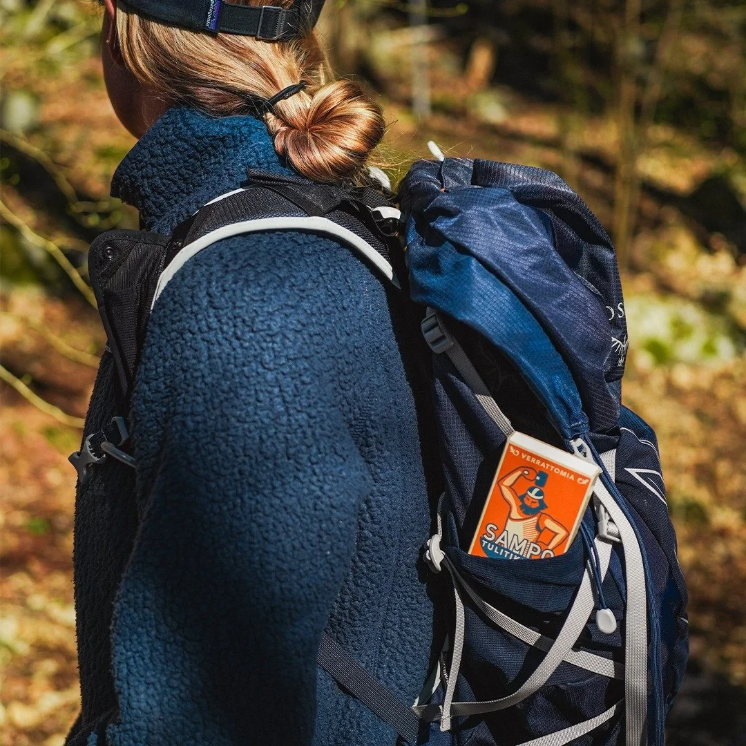 Side view of a person wearing a blue fleece jacket and a baseball cap, carrying a hiking backpack with a tag attached.