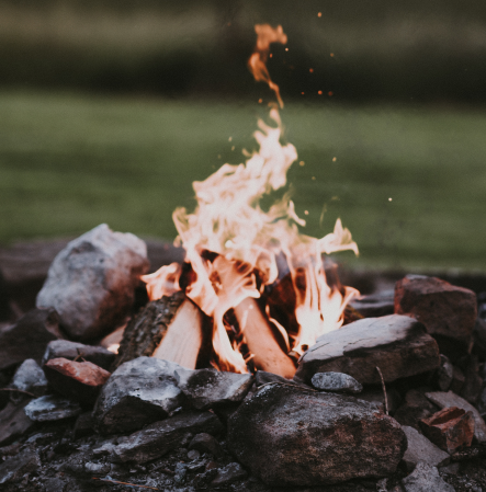 Campfire burning with logs and rocks around it outdoors.