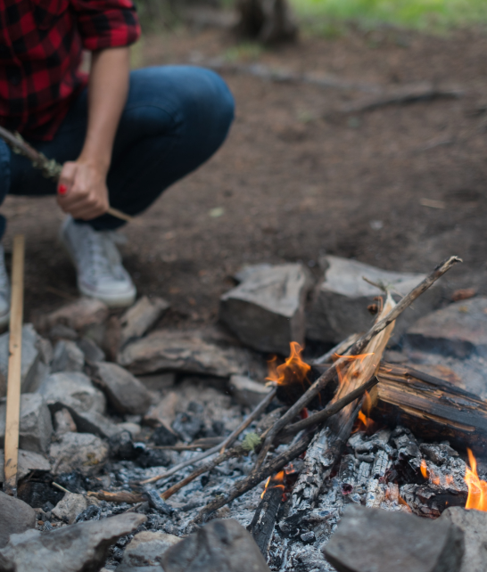 Person crouching near a campfire with rocks and sticks in outdoor setting.