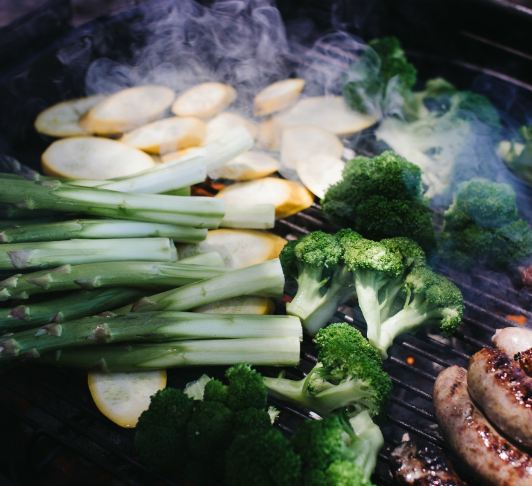 Asparagus spears, broccoli florets, sliced potatoes, and sausage links grilling on a barbecue