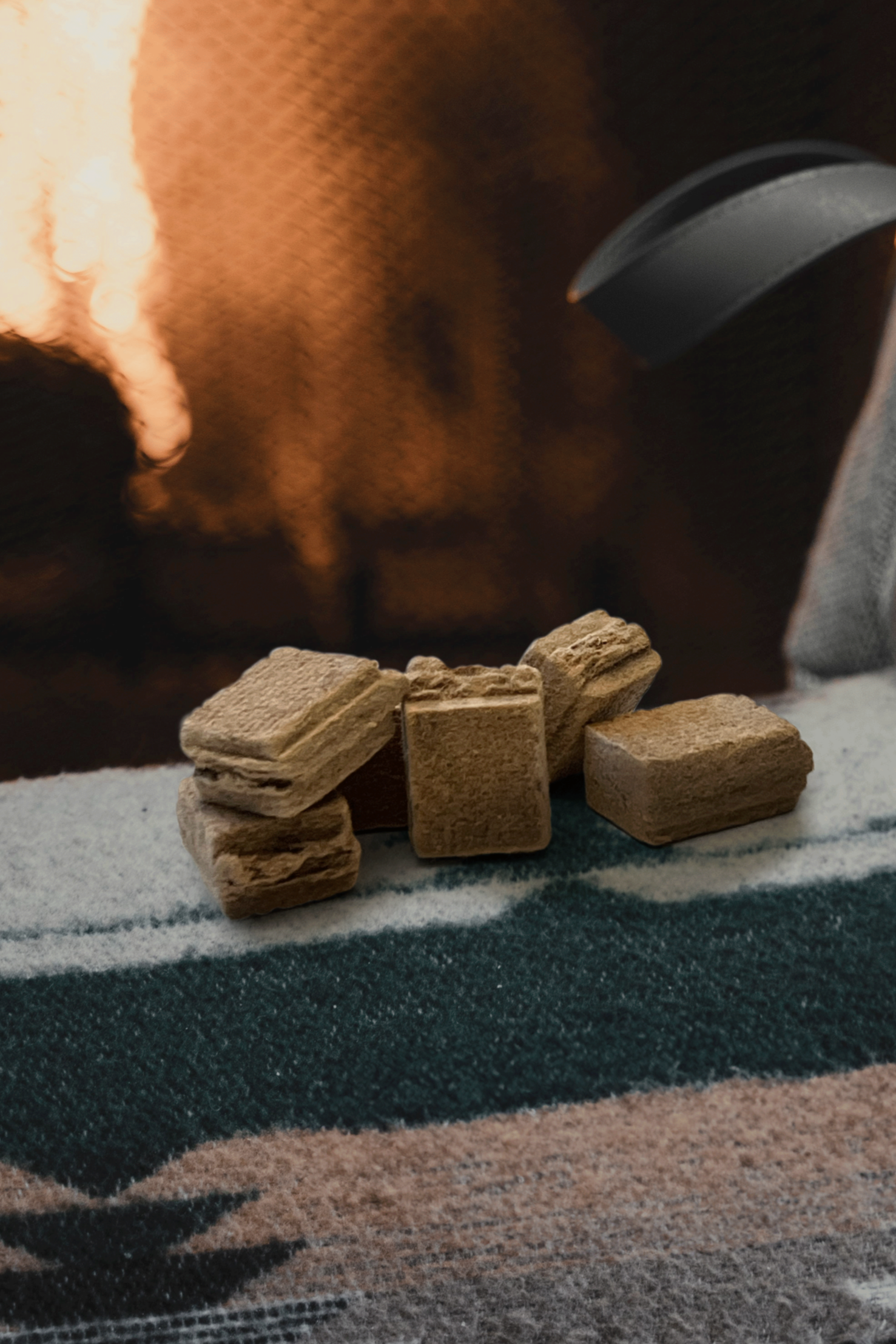 Fem små rektangulära beigefärgade stenar arrangerade på en yta med mörk bakgrund och en suddig ljuskälla.