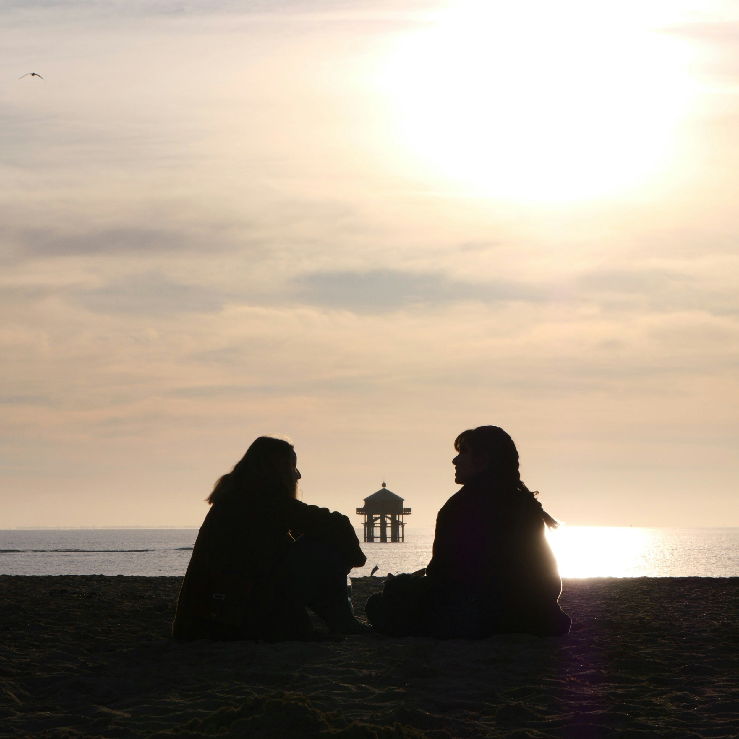 A silhouette of two talking women on the beach.