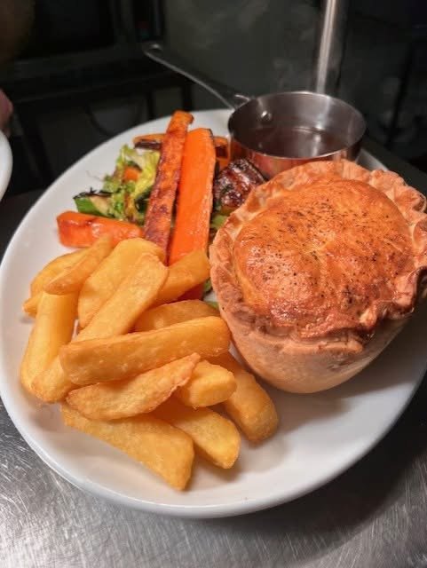 A plate of food with a baked potato topped with cheese, French fries, mixed vegetables, and a small cup of gravy.