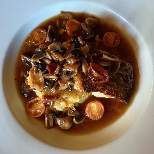 A bowl of cooked fish topped with sautéed mushrooms and sliced carrots in a brown broth.