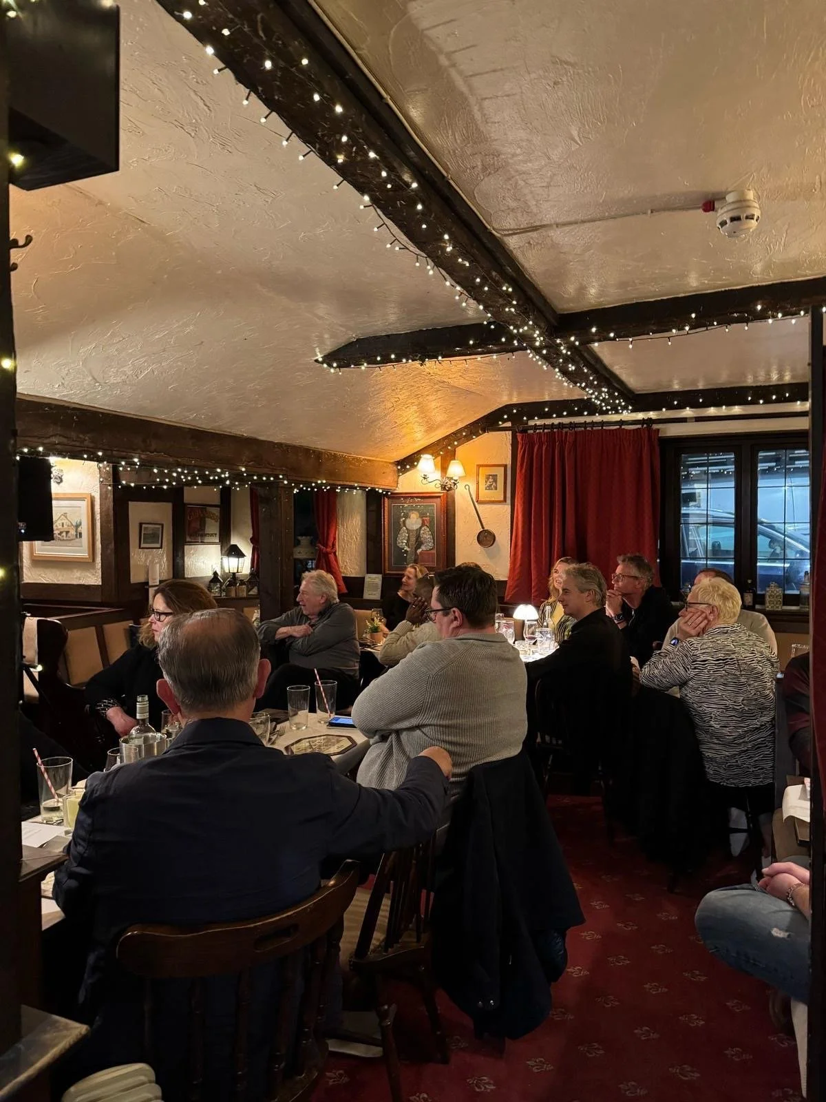People dining inside a cozy restaurant decorated with string lights hanging from the ceiling, framed pictures on the walls, and curtains covering the windows.