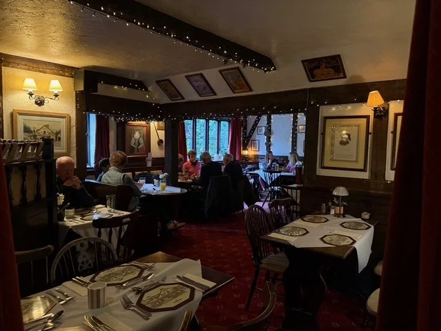 Interior of a cozy restaurant with several tables set with napkins and tableware, patrons dining, warm lighting, framed artwork on the walls, and fairy lights on the ceiling.