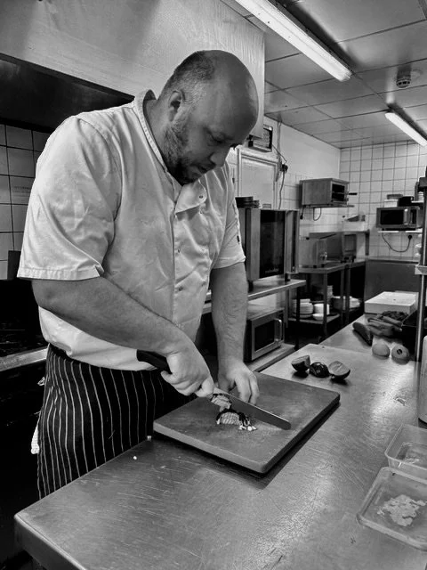 A chef in a white shirt and striped apron chopping vegetables on a cutting board in a professional kitchen.