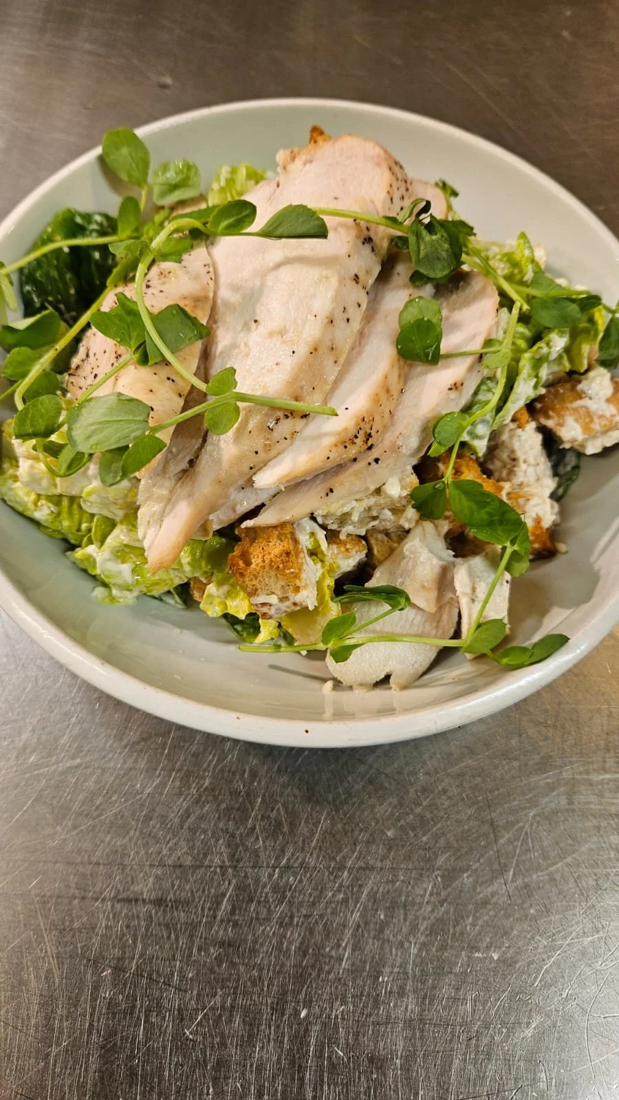 Bowl of grilled chicken slices on a bed of lettuce, topped with microgreens.