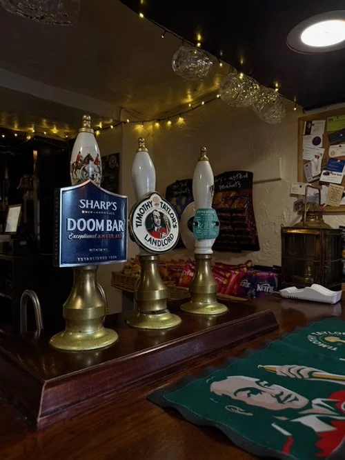 Three beer taps on a bar counter with decorative bottles and fairy lights overhead.