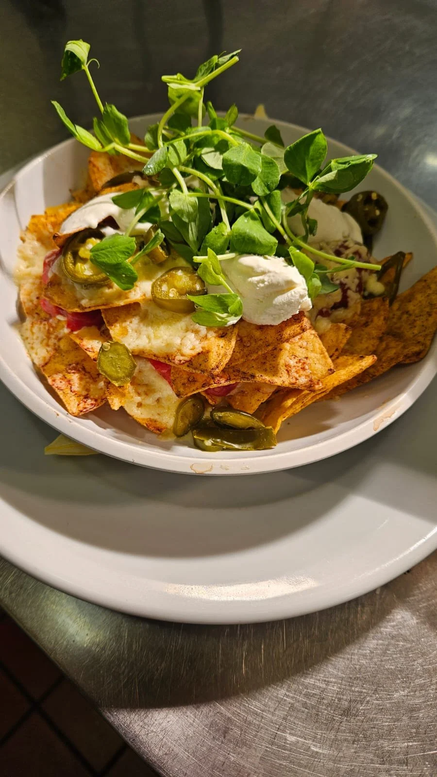 Bowl of nachos topped with green sprouts, sour cream, jalapeños, cheese, and meat.