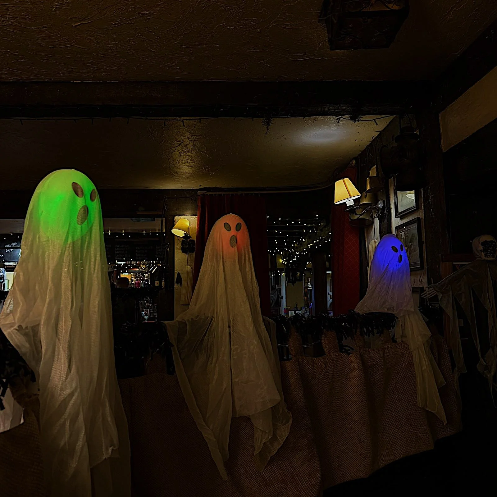 Halloween decorations of ghost figures with glowing heads in green, orange, and blue, displayed indoors with dim lighting.