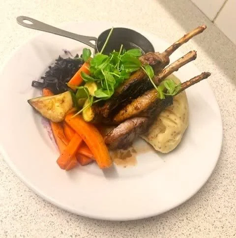 Plate of grilled lamb chops with roasted carrots, potatoes, and sautéed greens.