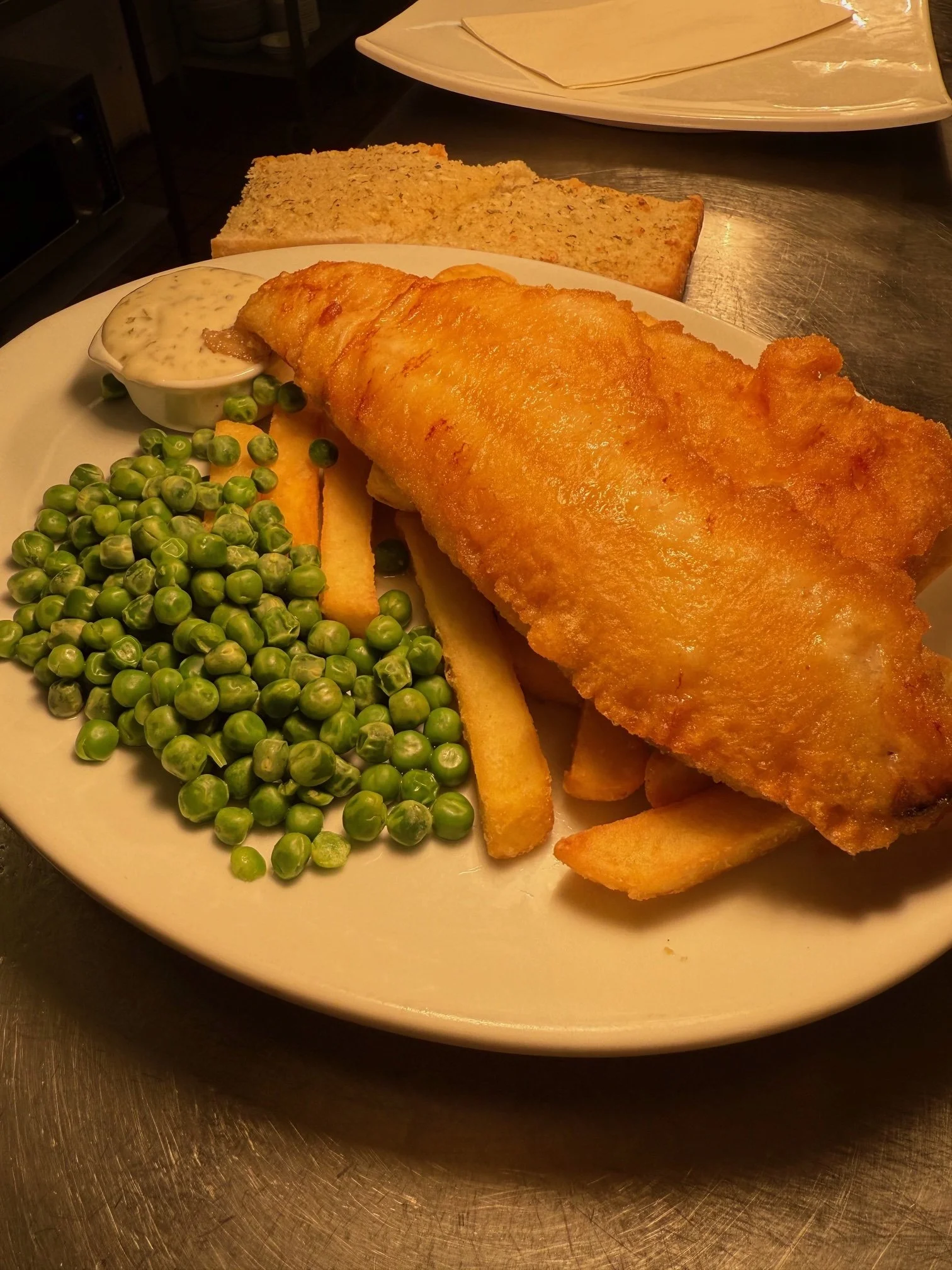 Evening menu. Plate of fish and chips with green peas, tartar sauce, and slices of bread in the background.