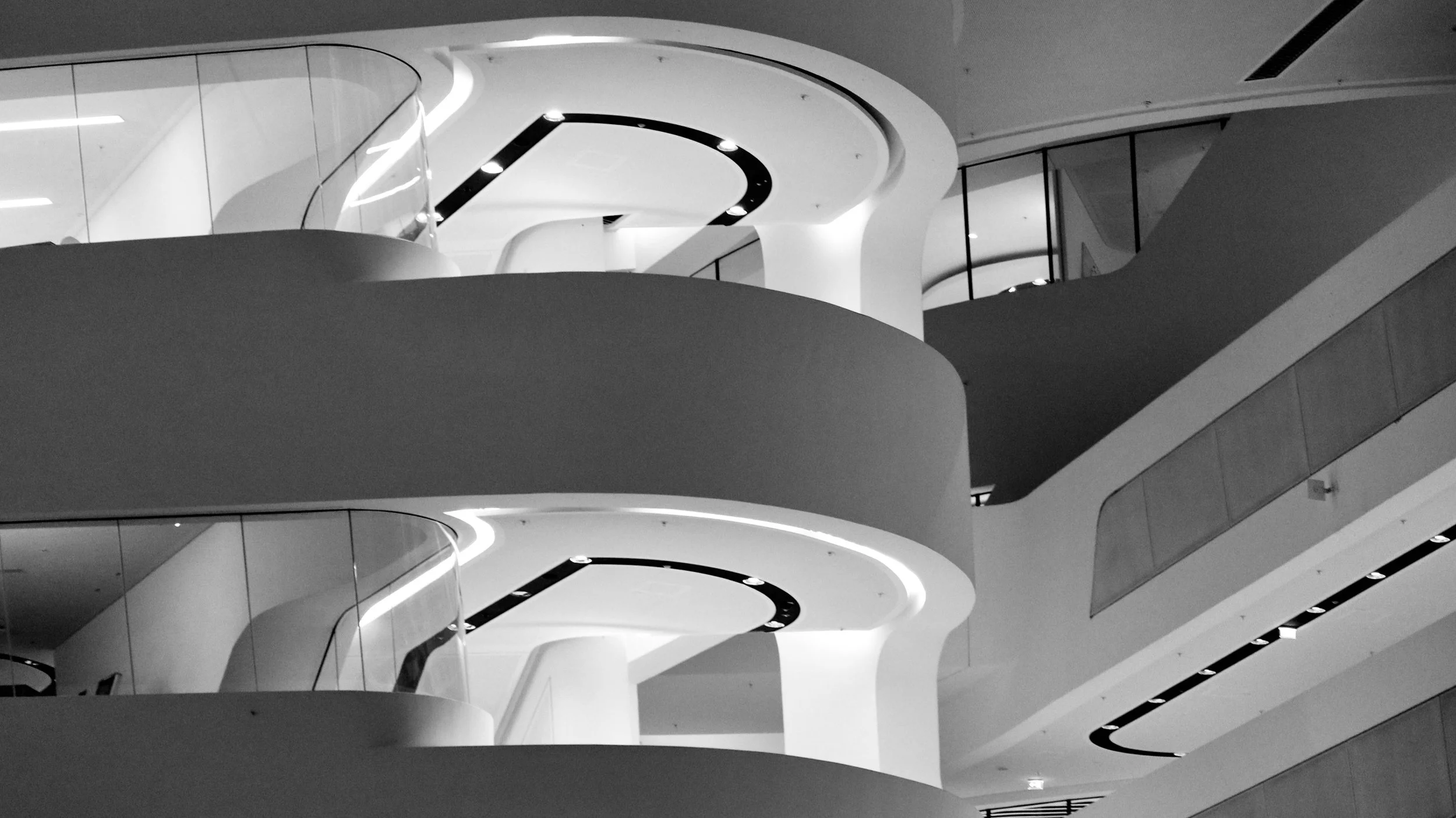 Schwarz-Weiß-Fotografie eines modernen, geschwungenen Innenarchitekturelements in einem Gebäude mit mehreren Etagen.