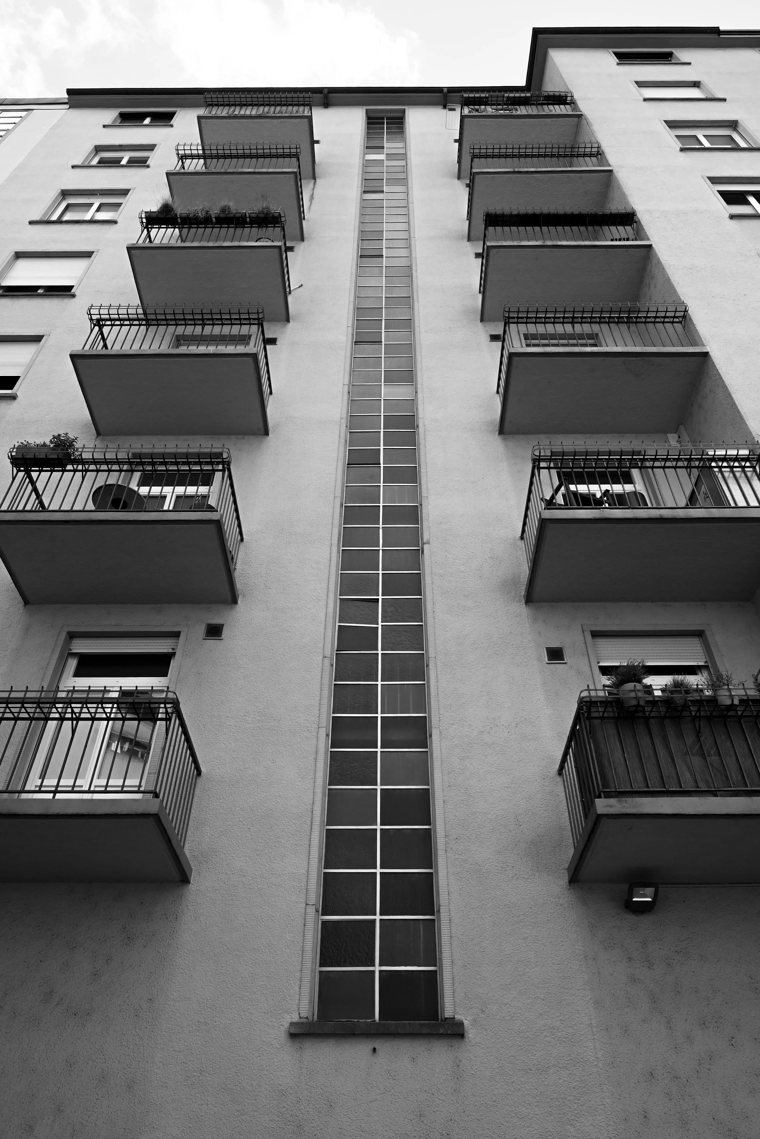 Aufnahmewinkel Blick nach oben auf ein mehrstöckiges Apartmentgebäude mit Balkonen auf der linken Seite, in Schwarz-Weiß-Fotografie.