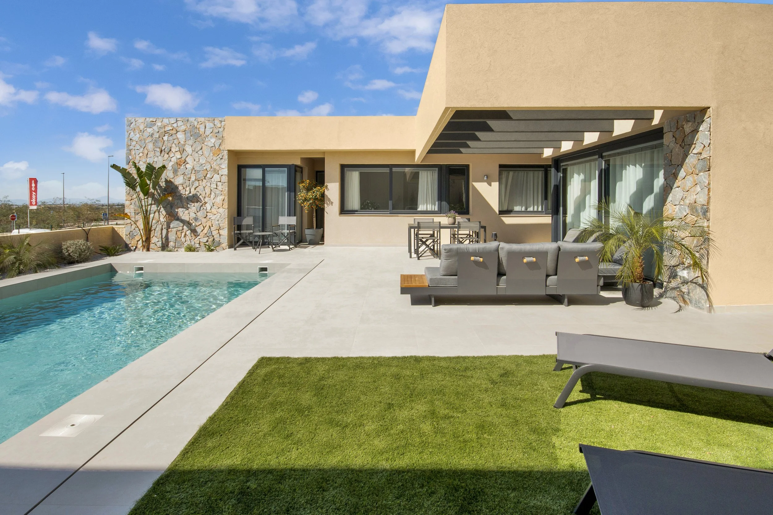 Modern backyard with a swimming pool, outdoor seating area, and green lawn under a clear blue sky.