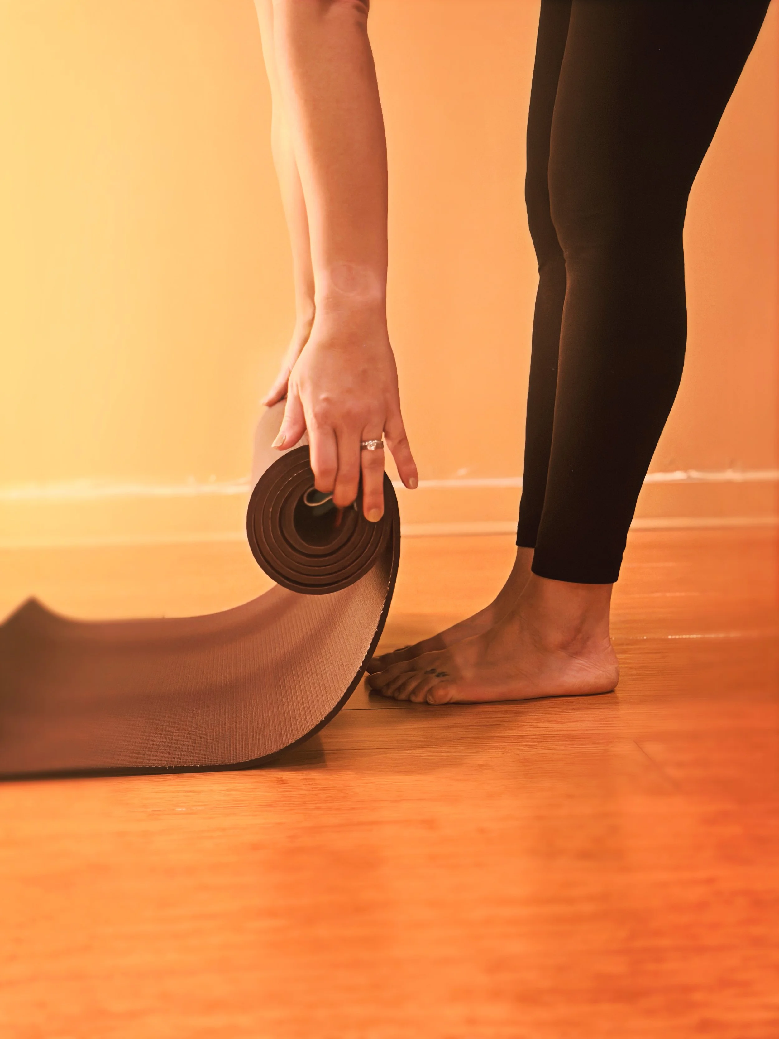Person rolling up a yoga mat on a wooden floor.