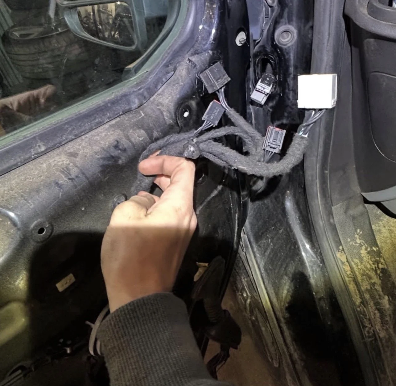 En person hanterar kablar i bilen, avlägsnad instrumentpanel eller dörrpanel, i en bils interiör.