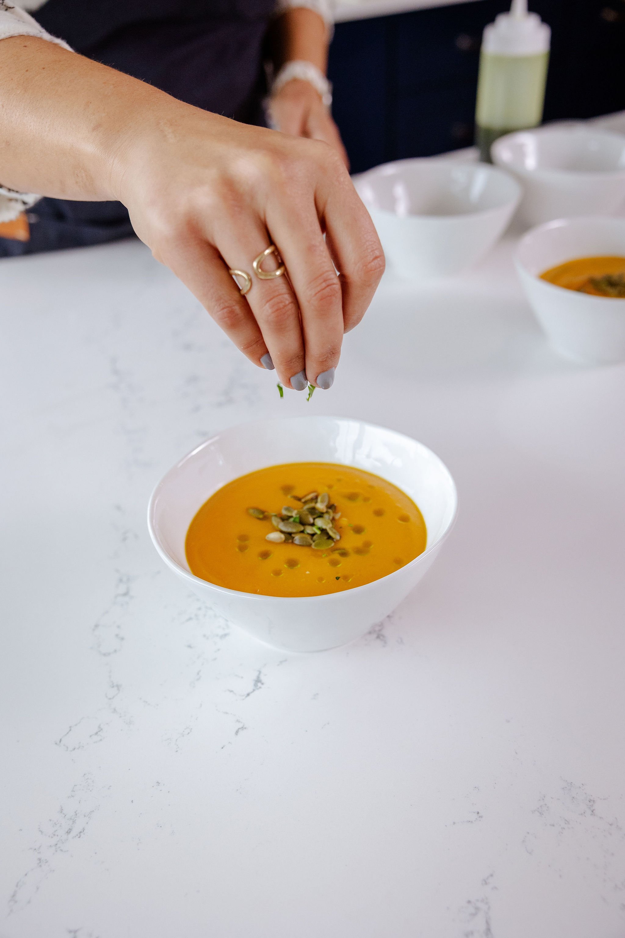 Chef Jenna Bethoney sprinkling green pumpkin seeds onto a bowl of butternut squash soup.