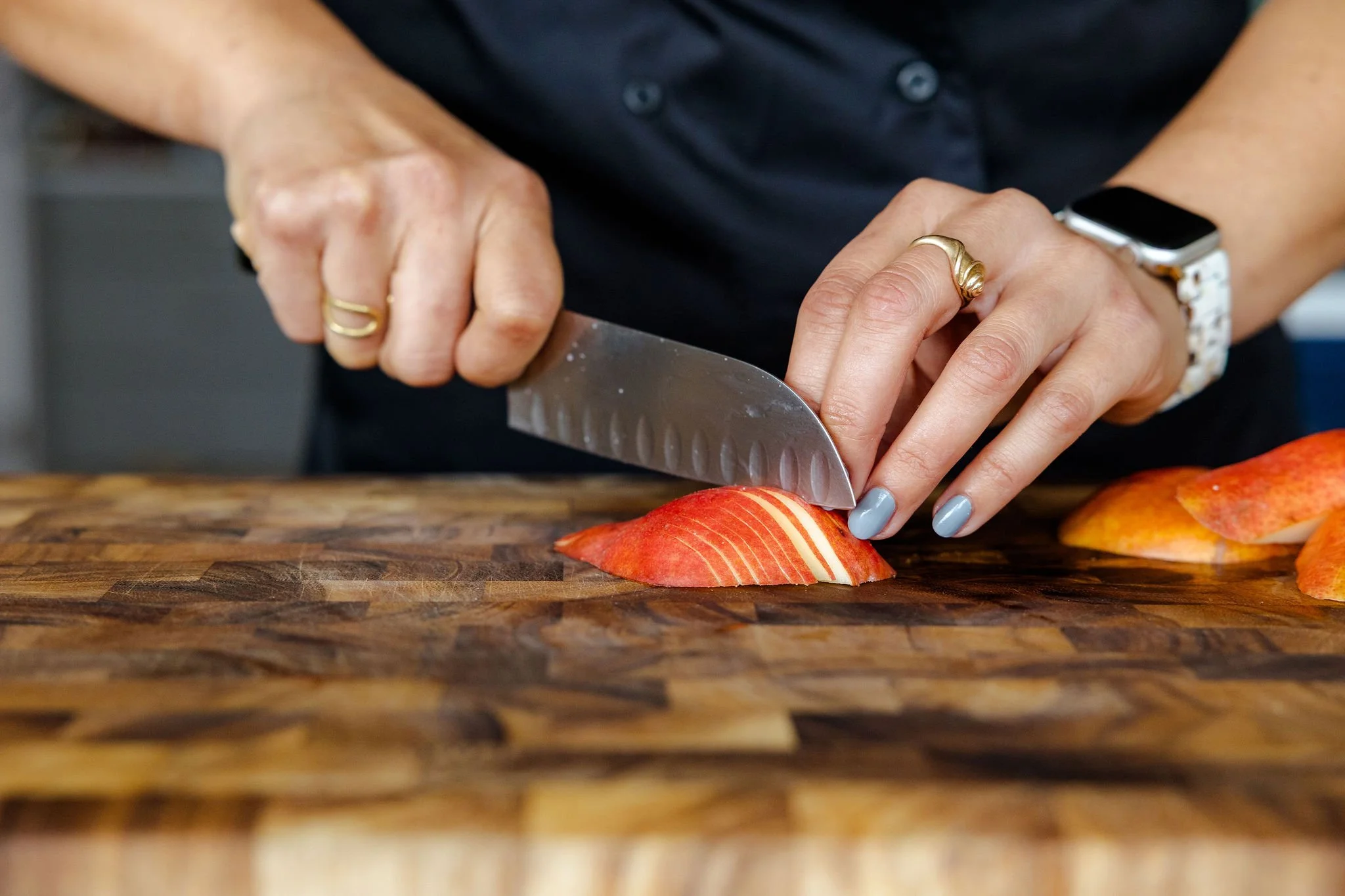 Chef Jenna Bethoney slicing a red pear on a Williams-Sonoma wooden cutting board with a Wustof Santoku knife.