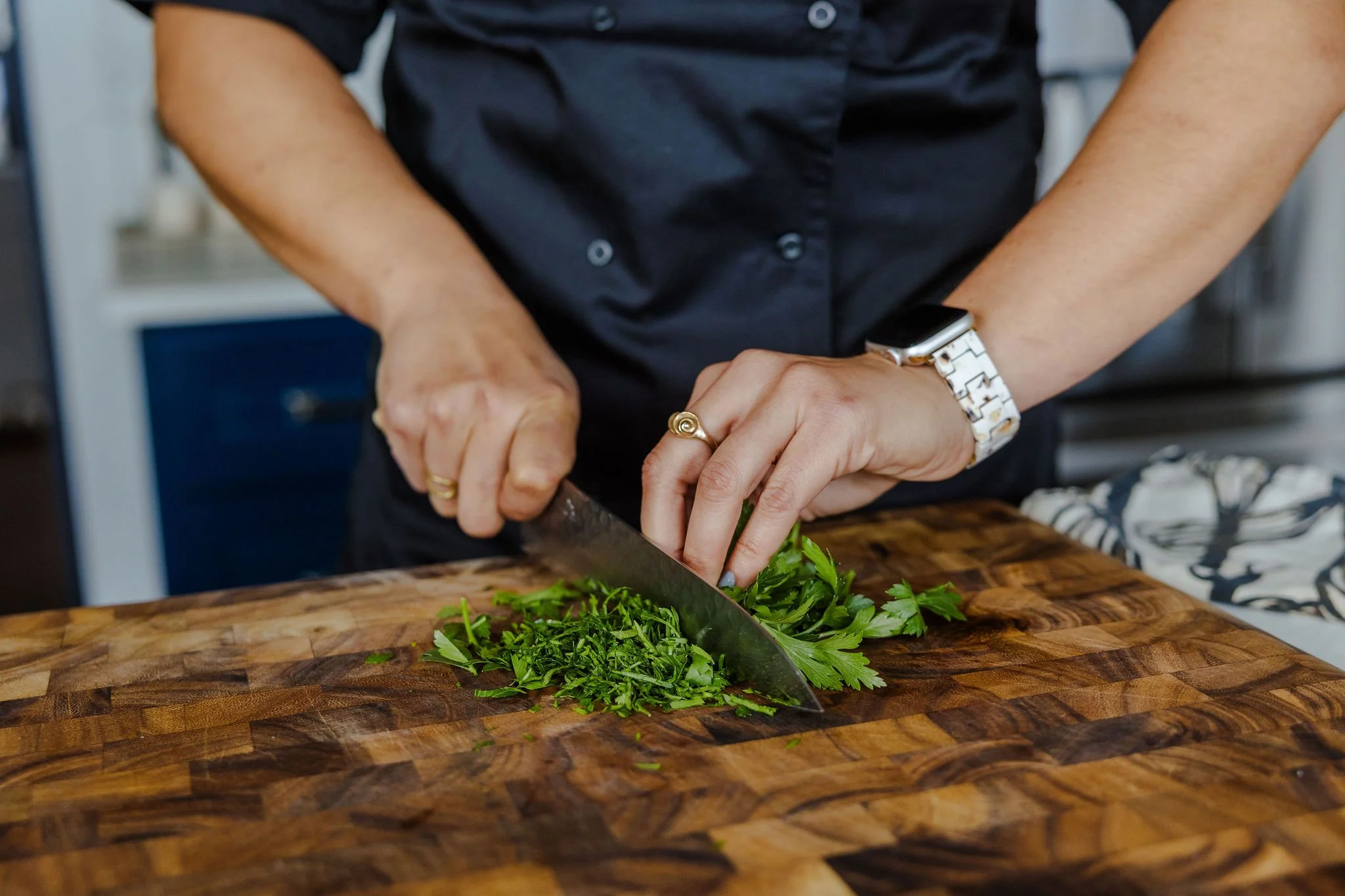 Chef Jenna Bethoney chopping fresh green parsley on a wooden cutting board.