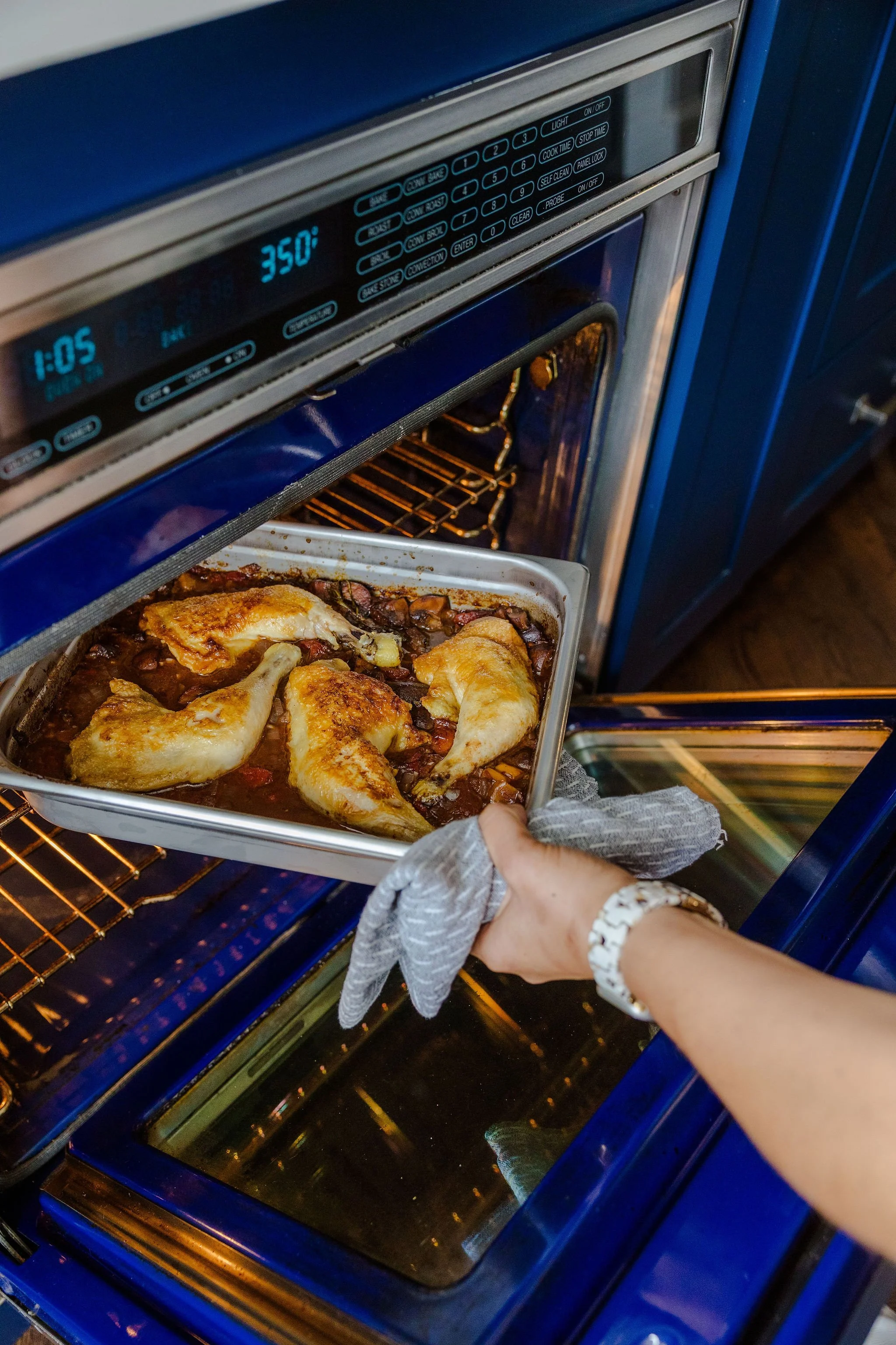 Chef Jenna Bethoney placing a tray of Chicken Cacciatore into an oven.