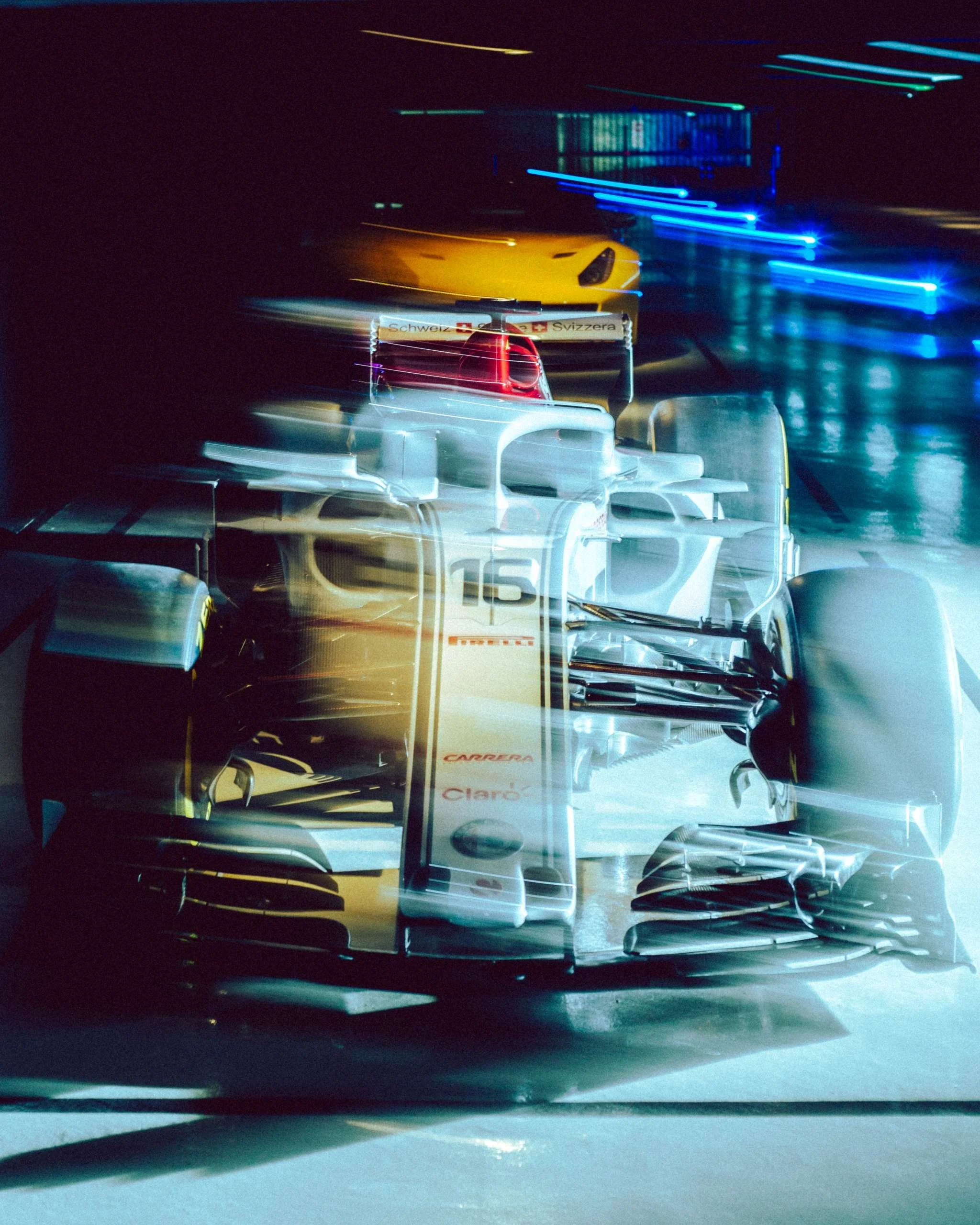 voiture de course de Formule 1 à l'intérieur d'un paddock, prise en rafale ou à longue exposition avec des lumières bleues et jaunes environnantes