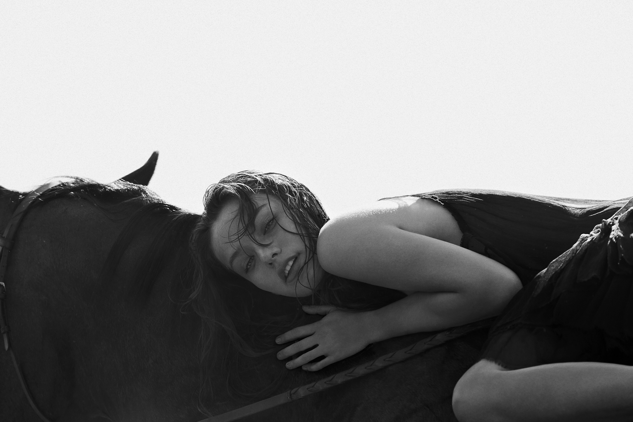 Une femme aux cheveux mouillés repose sur le corps d'un cheval.