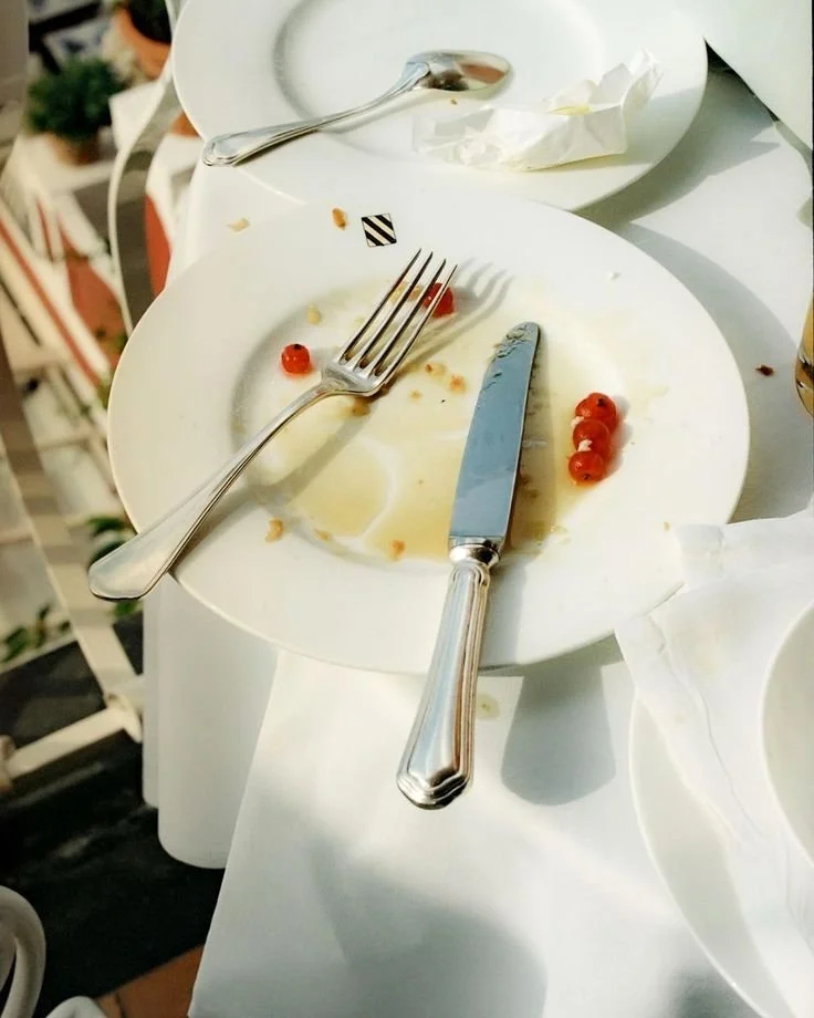 Assiette vide avec quelques restes de nourriture et fruits rouges, couvert et couteau dessus, sur une table blanche