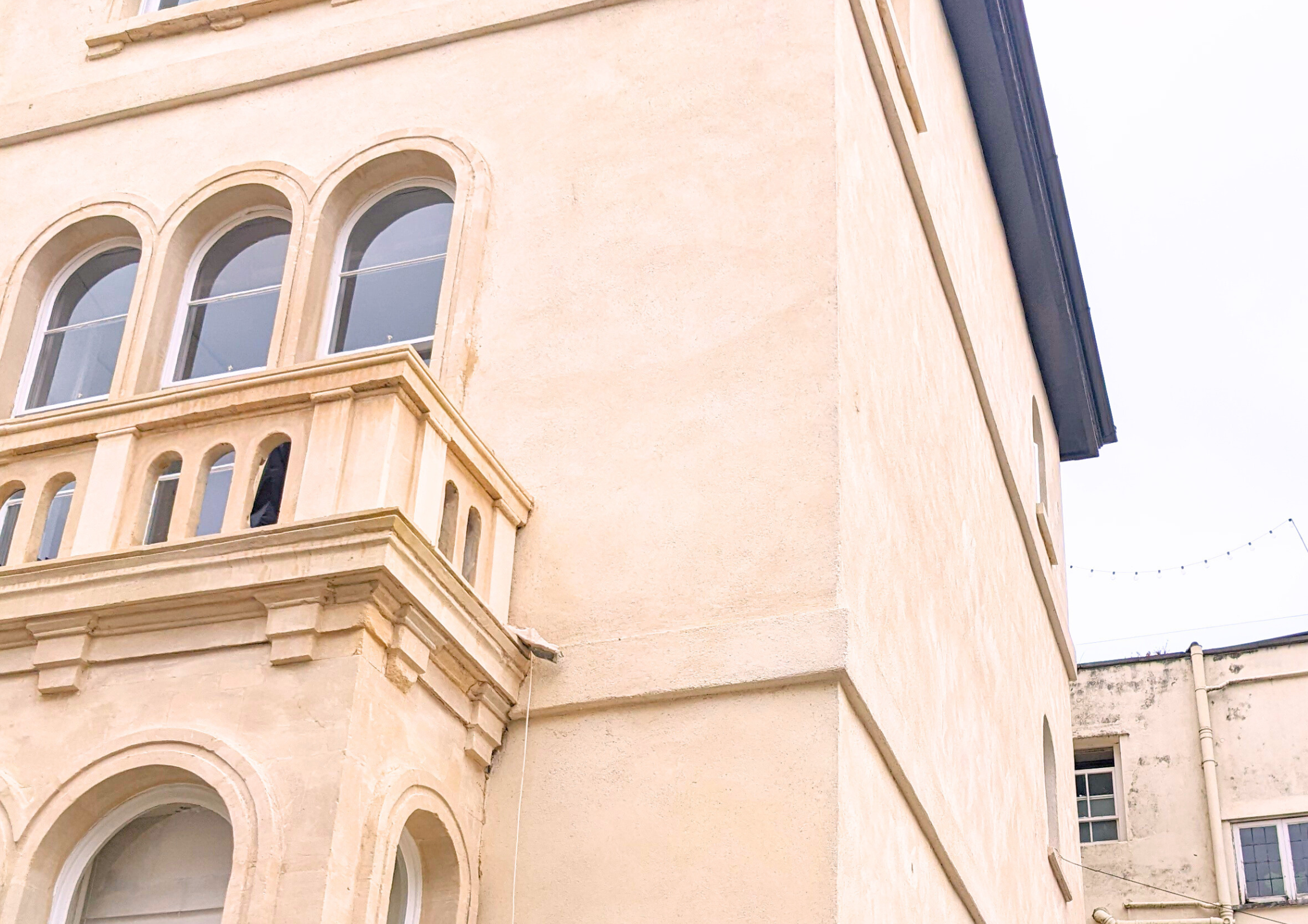 Close-up view of a beige building with arched windows and decorative balcony railing, showing part of the upper floors.