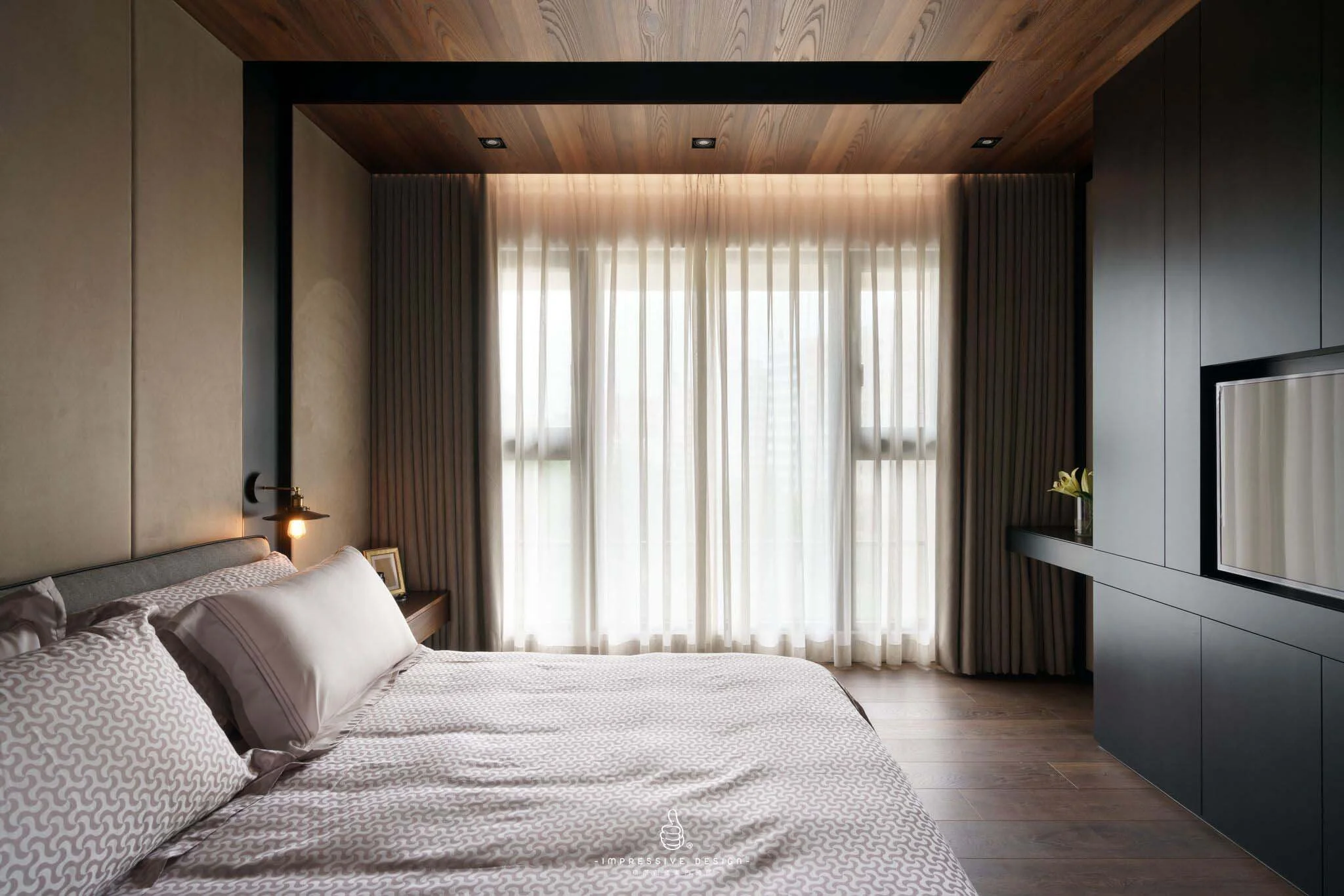 Modern bedroom with large window covered by sheer white curtains, dark wood accents, a bed with geometric patterned bedding, and built-in black cabinets.