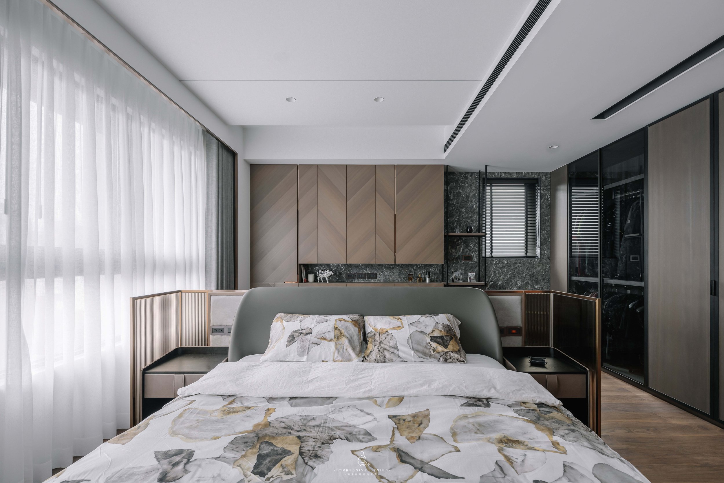 Modern bedroom with large bed, marble-patterned bedding, and a mix of wood and stone decor, with large windows and curtains.
