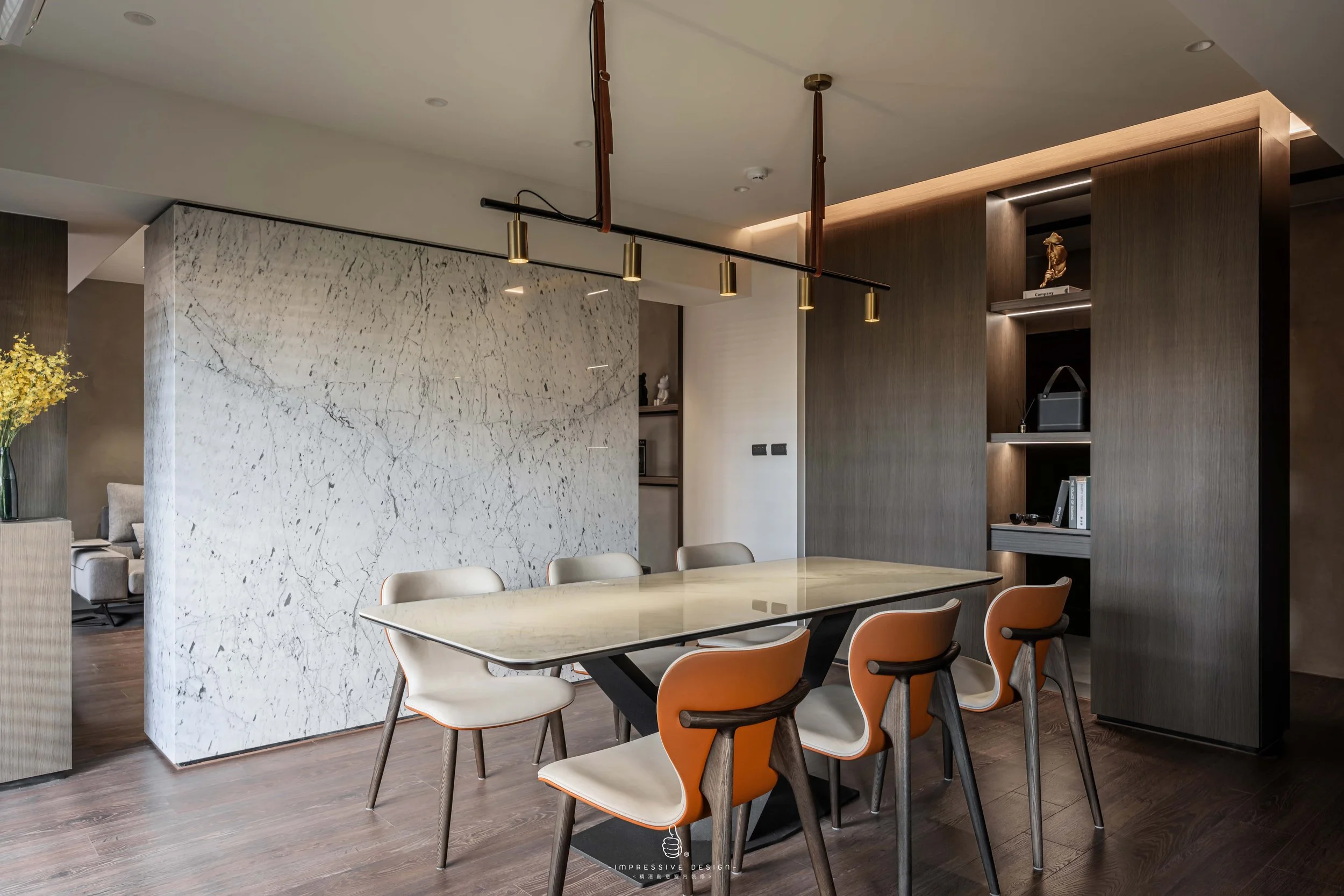 Modern dining room with a marble table, six chairs, dark wooden wall unit, and gold lighting fixture.