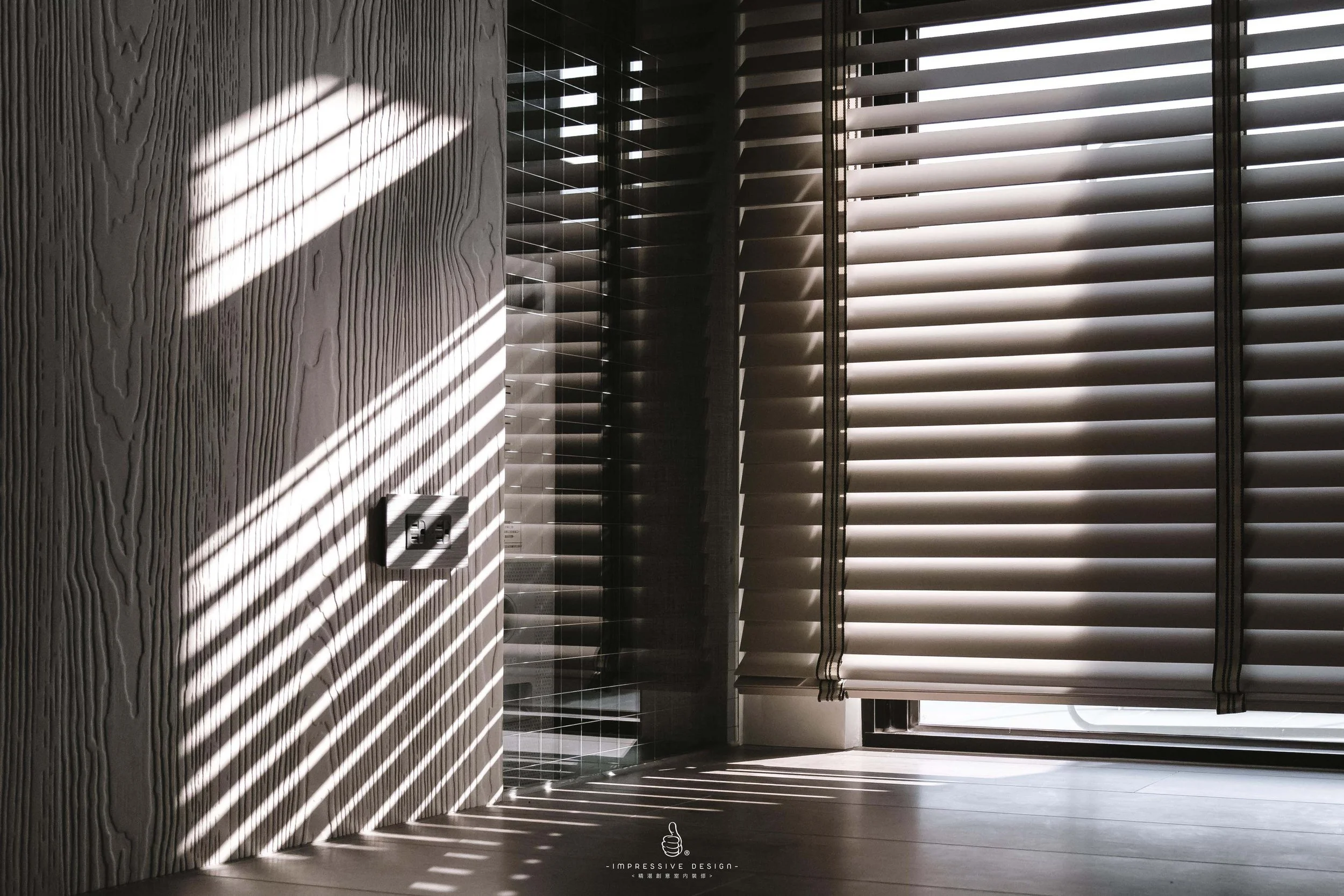 Sunlight coming through horizontal blinds, casting striped shadows on a textured wall and floor, with electrical outlets visible on the wall.