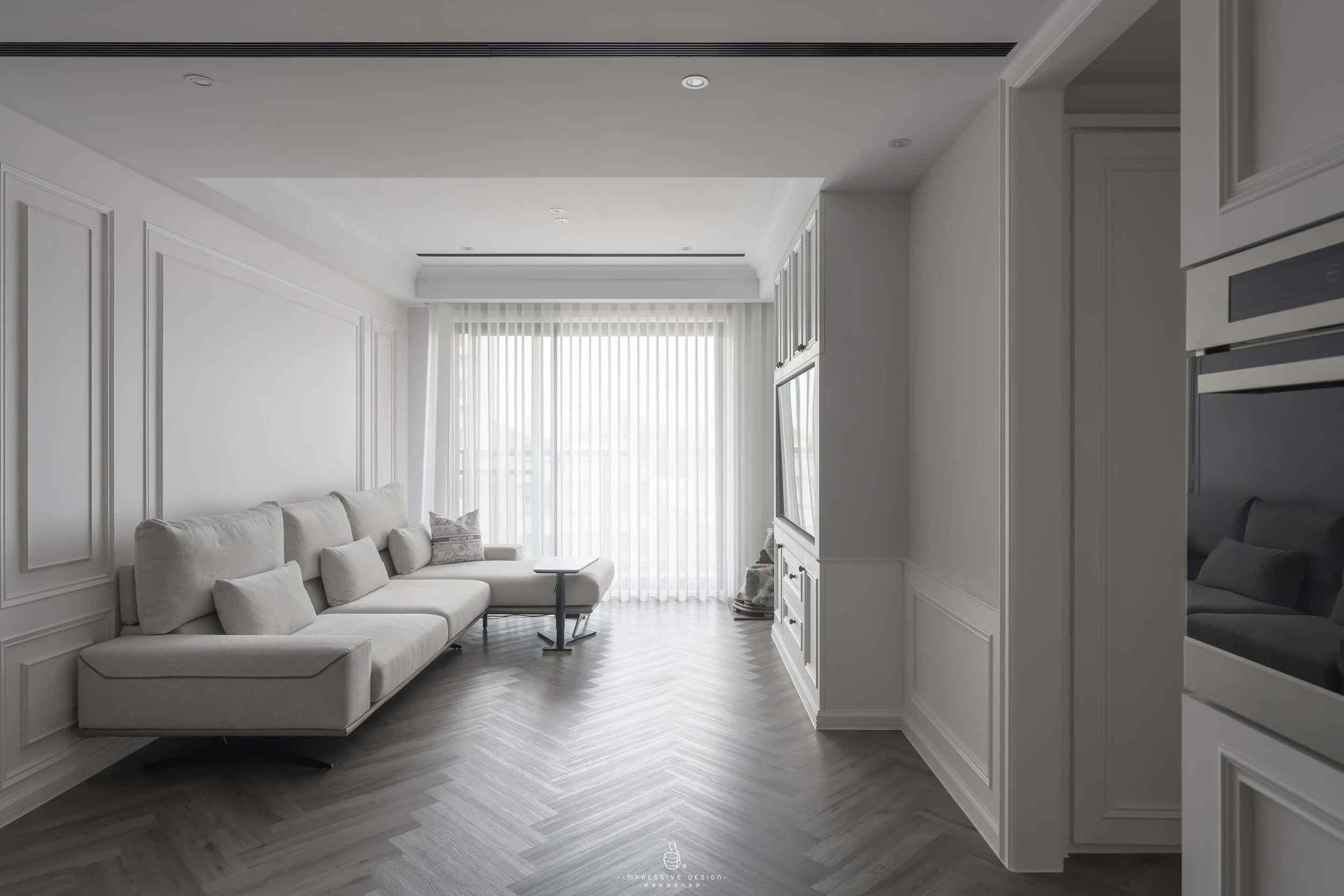 Bright living room with white walls, a white sectional sofa, a window with sheer white curtains, and a TV mounted on the wall.