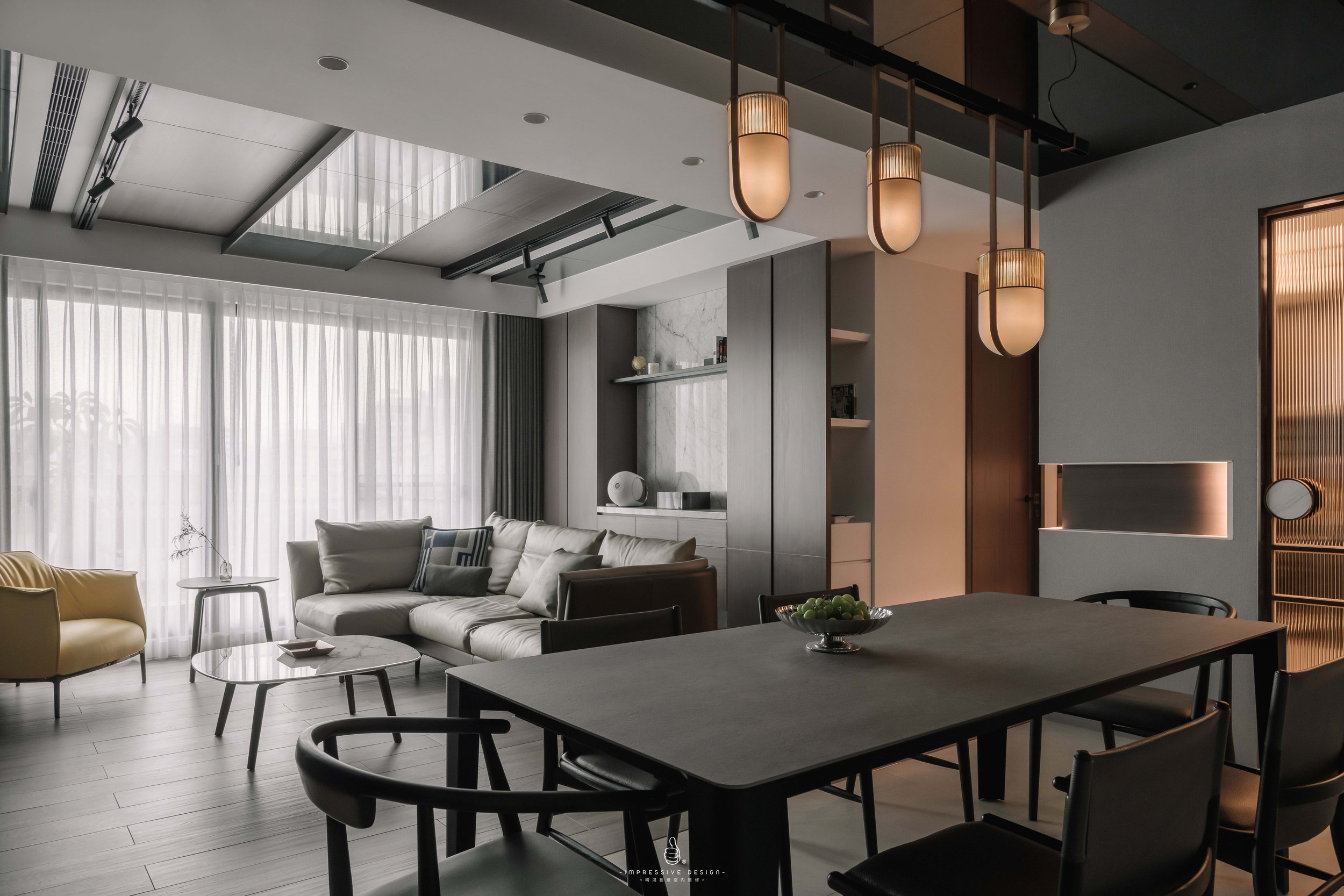 Modern living room and dining area with gray and beige tones, large window with sheer curtains, beige sofa with pillows, yellow armchair, coffee tables, black dining table with chairs, pendant lighting, minimalist decor.