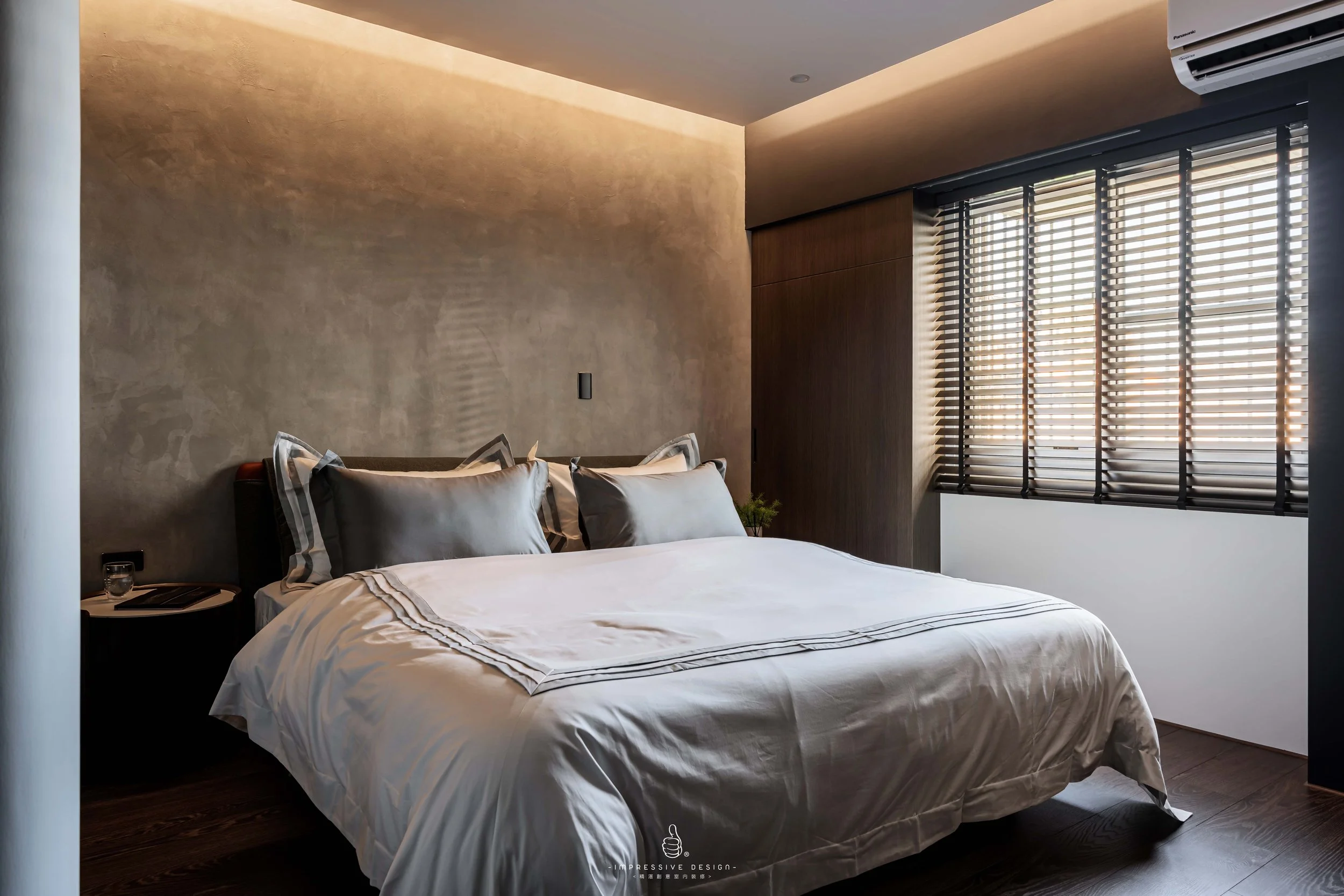 Modern bedroom with a bed, gray and white bedding, and black window blinds.