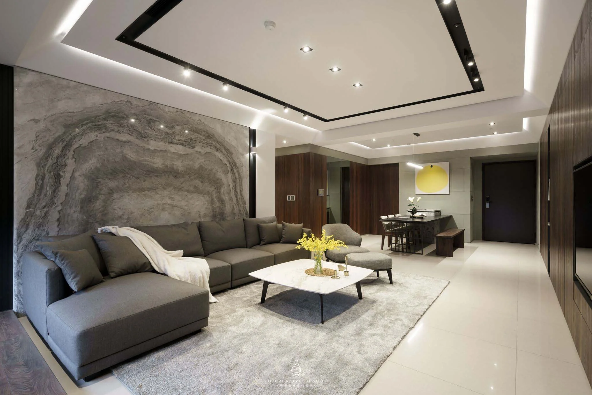 Modern living room with gray sectional sofa, marble coffee table with yellow flowers, textured wall art, tatami mats, and a dining area with yellow artwork.