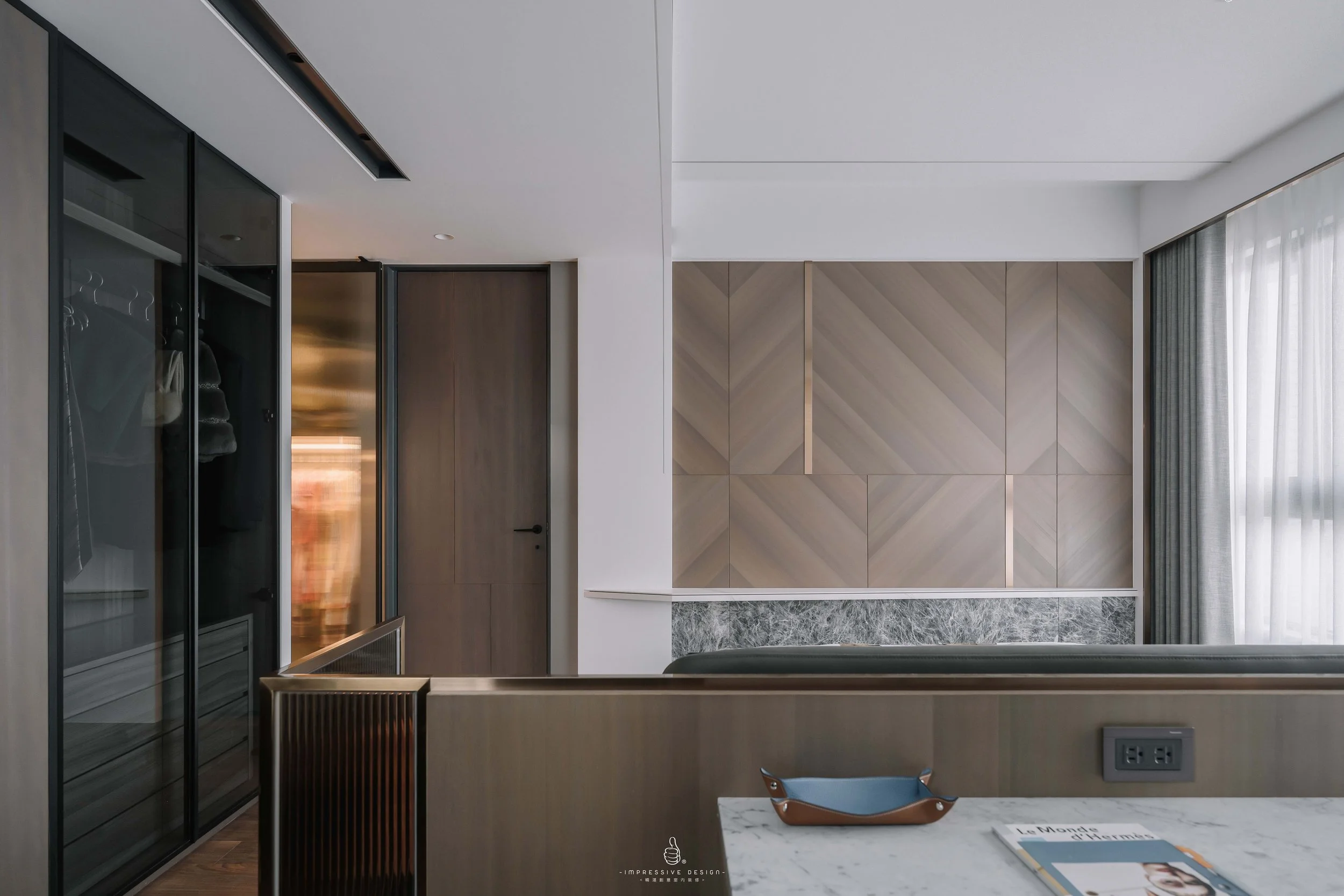 Modern interior room with a sideboard, marble top, and a tray. Light wood panel wall behind a sofa and large window with sheer curtains. Closet with glass doors and a closed wooden door.