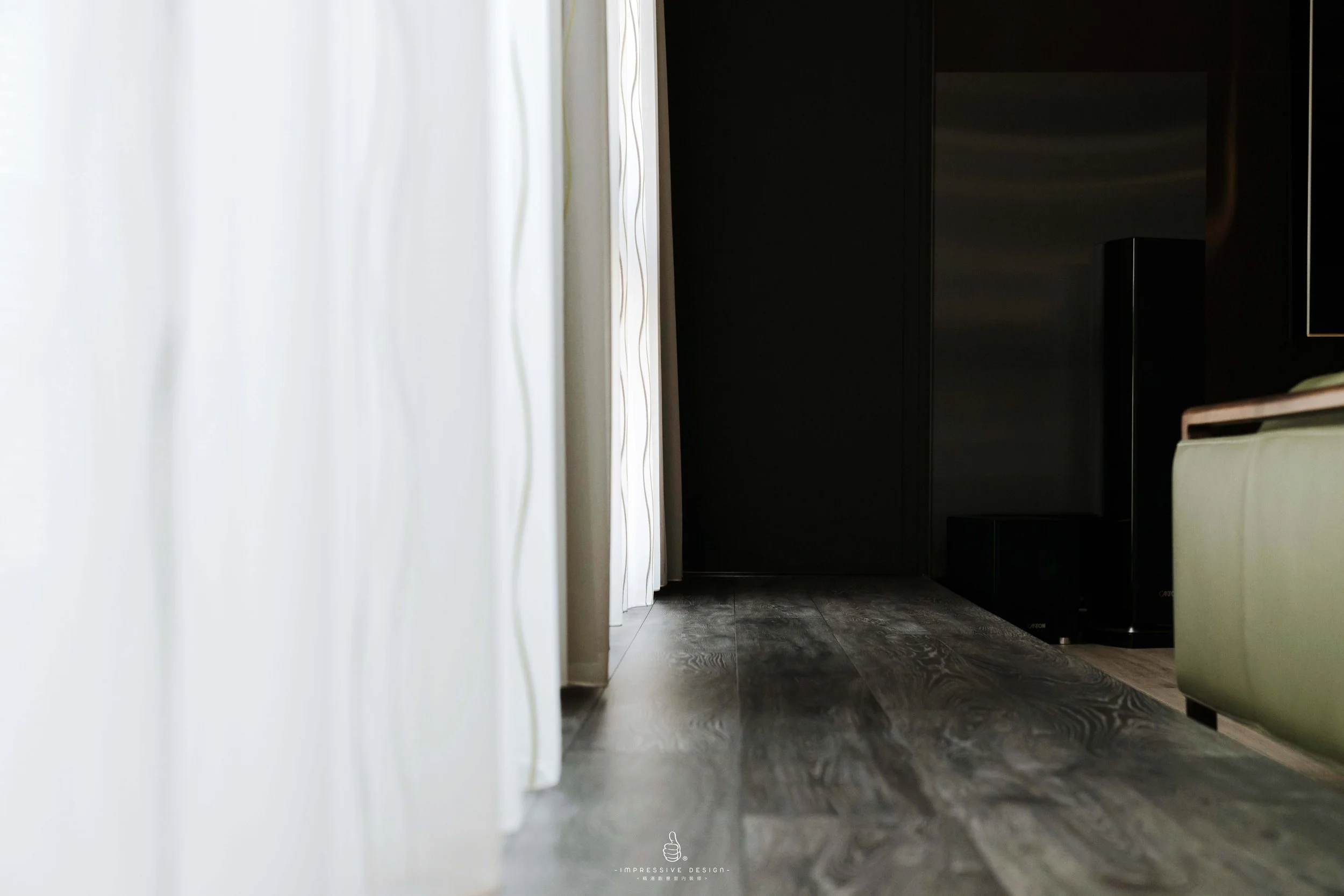 Photo of a dark hallway with a white curtain on the left and black cabinets or walls on the right, with a wood-patterned floor.
