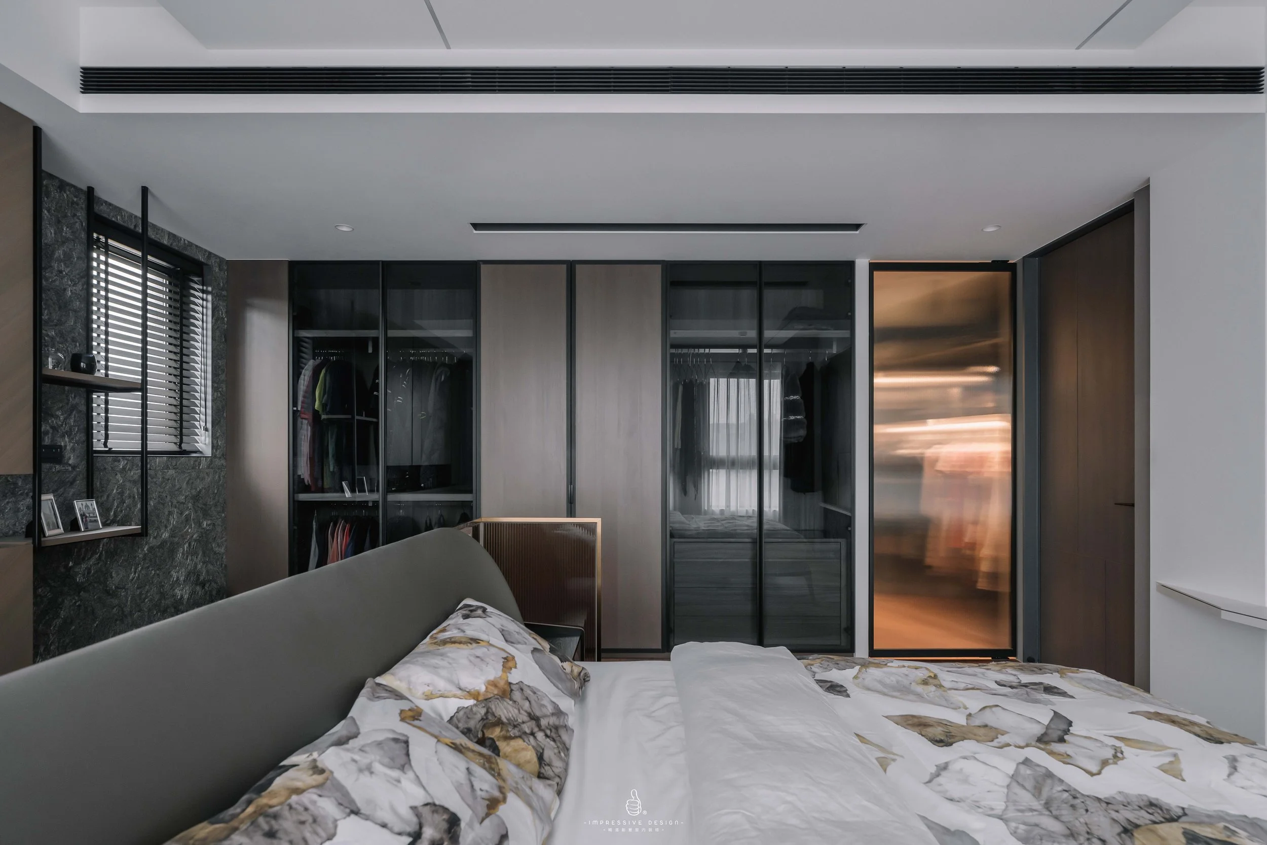 Modern bedroom with a bed featuring marble-patterned pillows in the foreground, an open closet with clothes behind glass doors, a window with blinds, and a sliding door with a blurred motion effect reflecting sunlight.