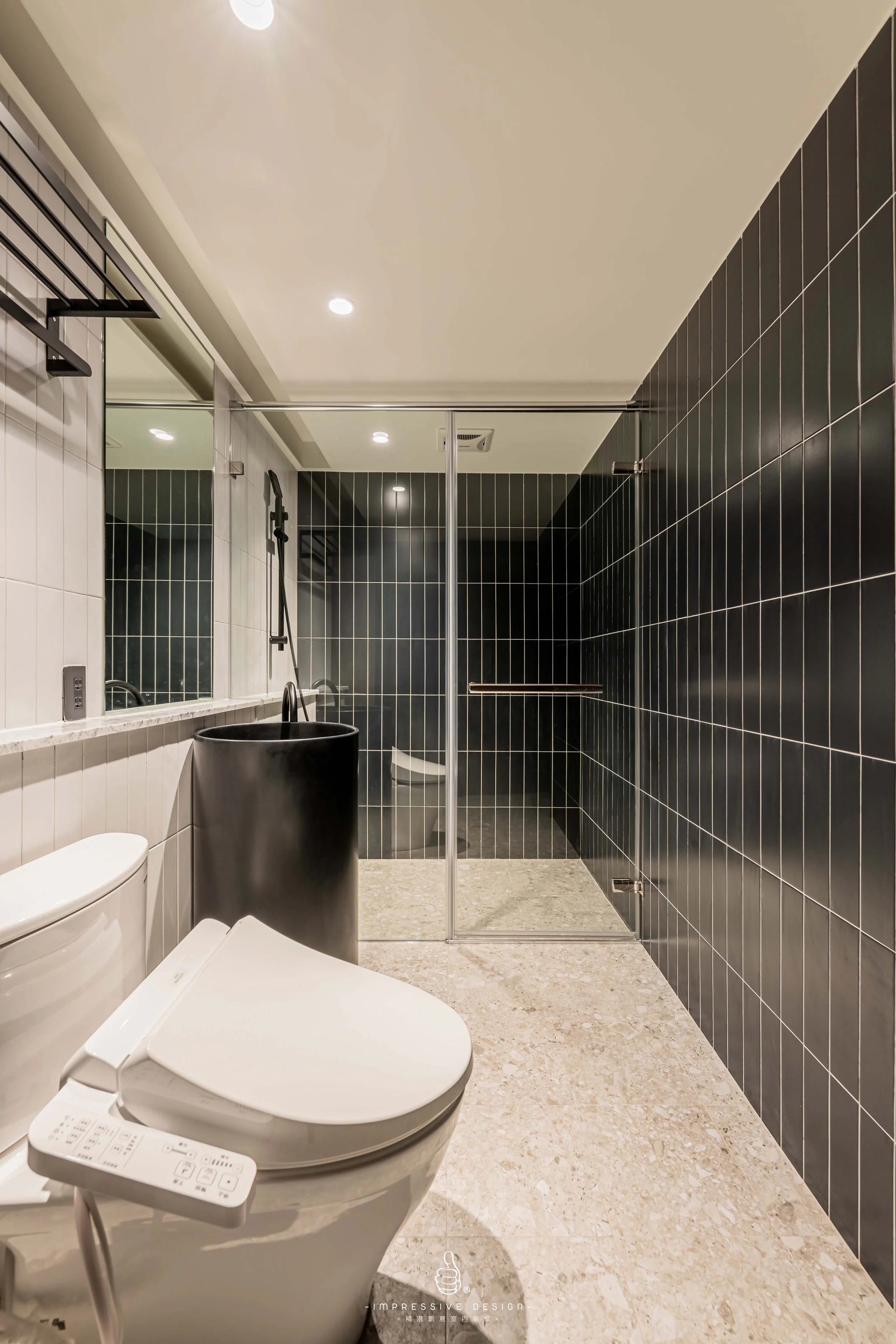 Modern bathroom with a white toilet, black sink, large mirror, and a glass-enclosed shower area with black tiles.