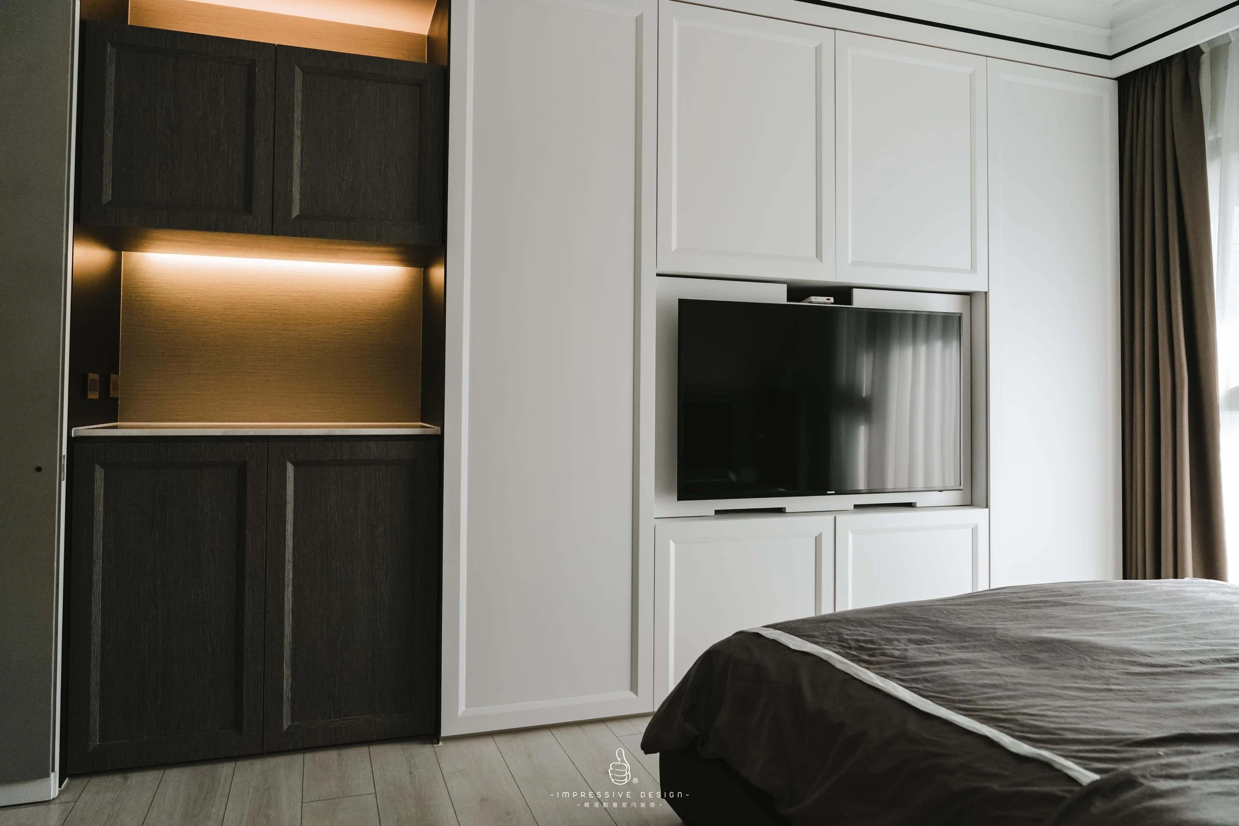 A modern hotel room with a dark and white wardrobe, flat-screen TV, bed, and a window with curtains.