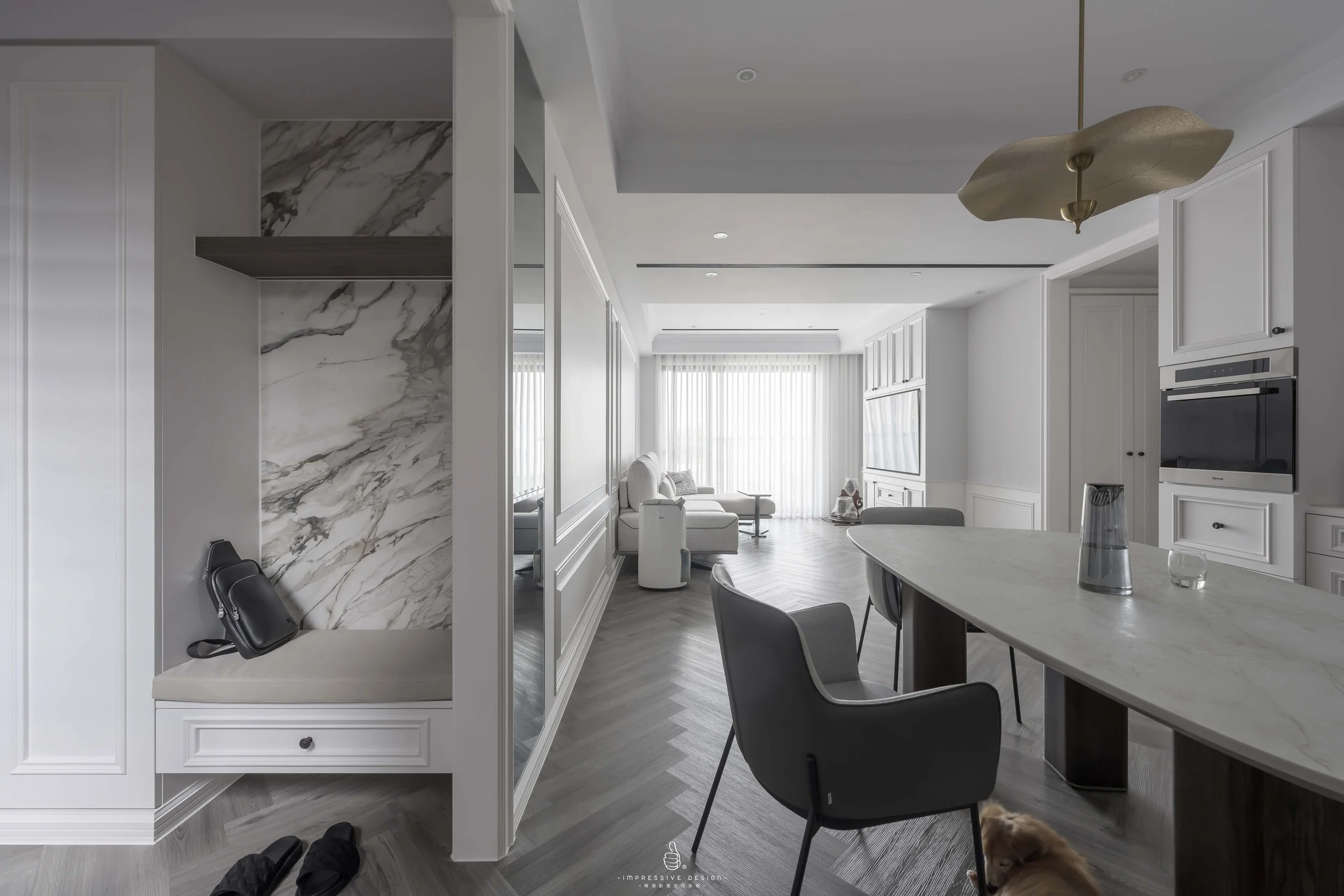 Modern, open-concept living room and kitchen with white walls, grey wooden floors, and large windows with vertical blinds. The kitchen includes white cabinetry, a marble countertop, and a built-in microwave. The lounge area features a white sofa, a T
