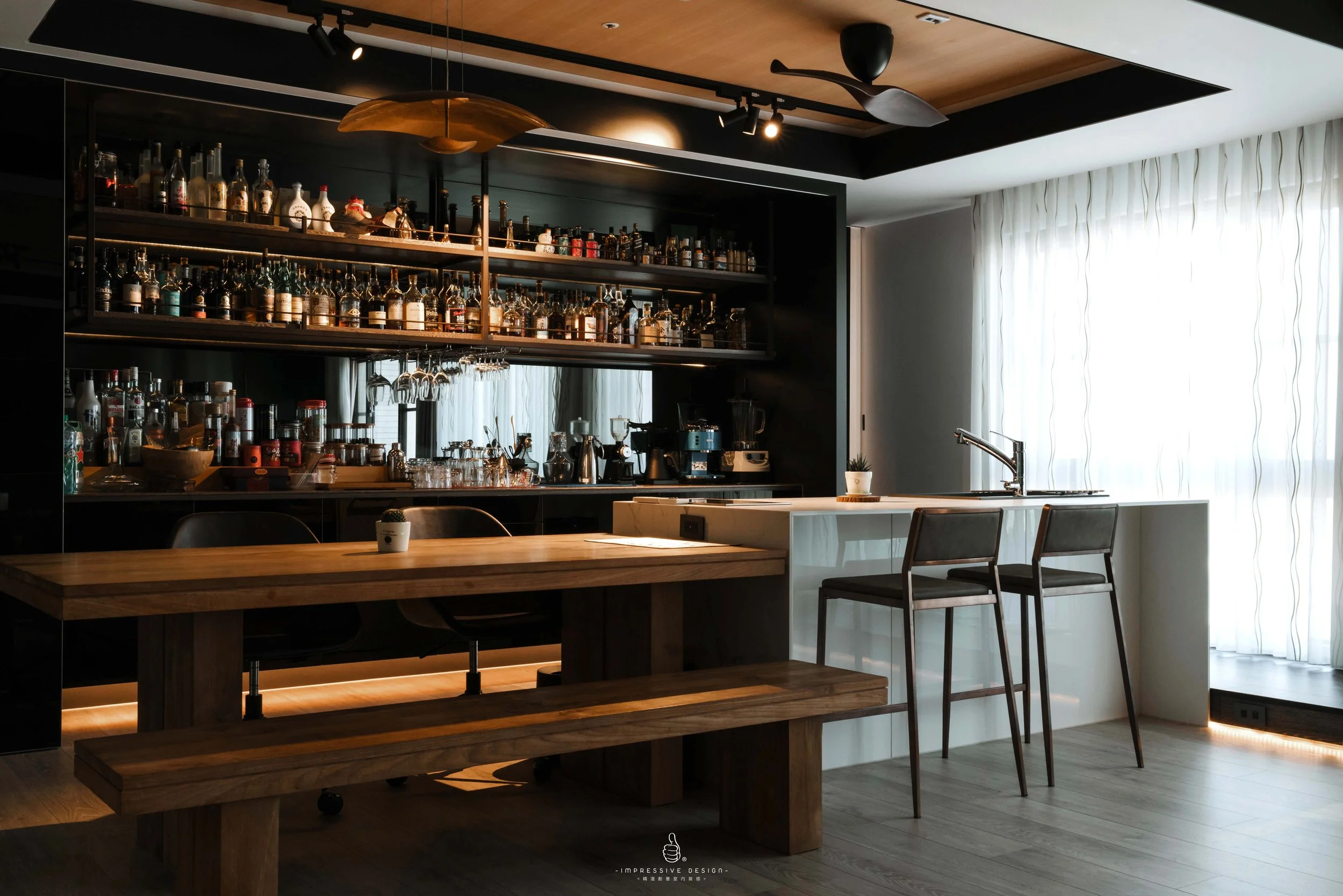 Modern bar area with a wooden counter, black shelving filled with liquor bottles, a coffee machine, and bar stools near a large window with sheer curtains.
