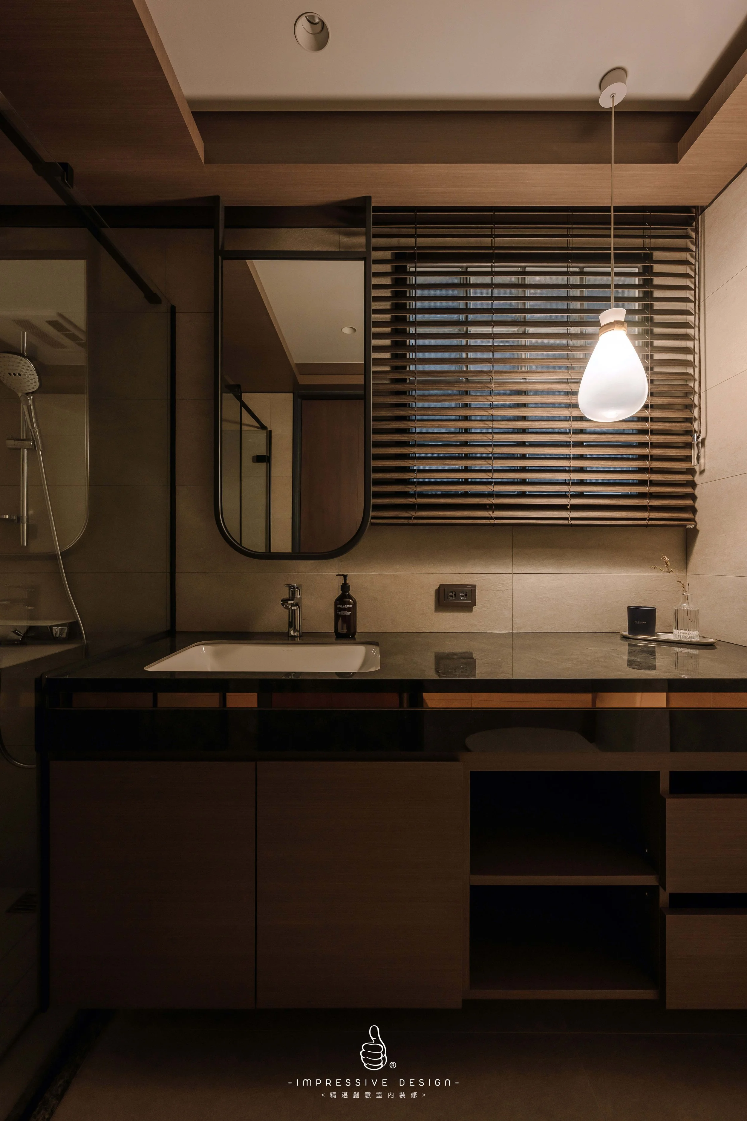 A modern bathroom with a black countertop, a white sink, a black soap dispenser, a mirror, a window with wooden blinds, a hanging light fixture, and decorative items on the counter.