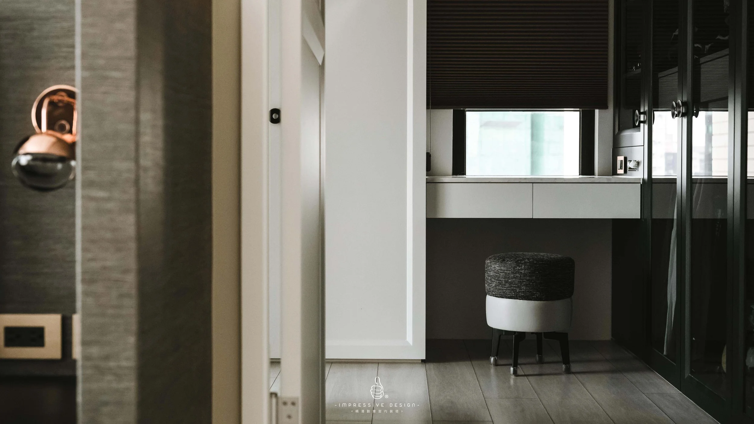 Modern kitchen or workspace with a white cabinet, black window blinds, a small black and white stool, and black storage cabinets with glass doors.