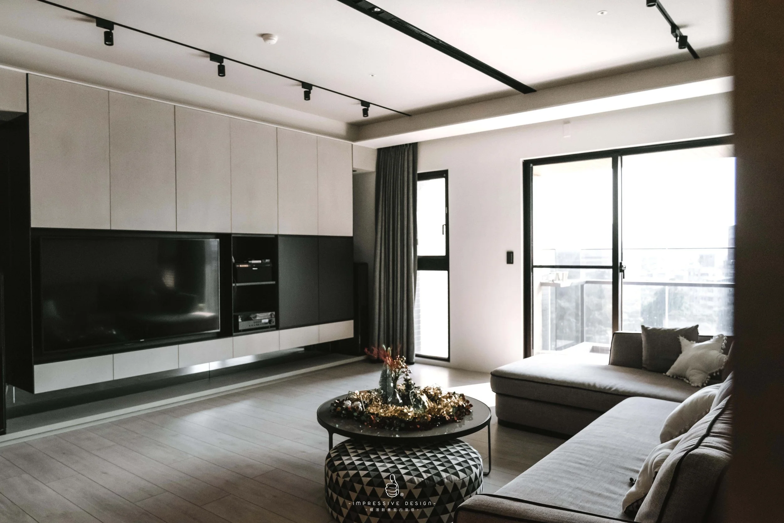 Modern living room with a wall-mounted TV, a sliding glass door leading to a balcony, a beige sofa, and a round coffee table with holiday decorations.