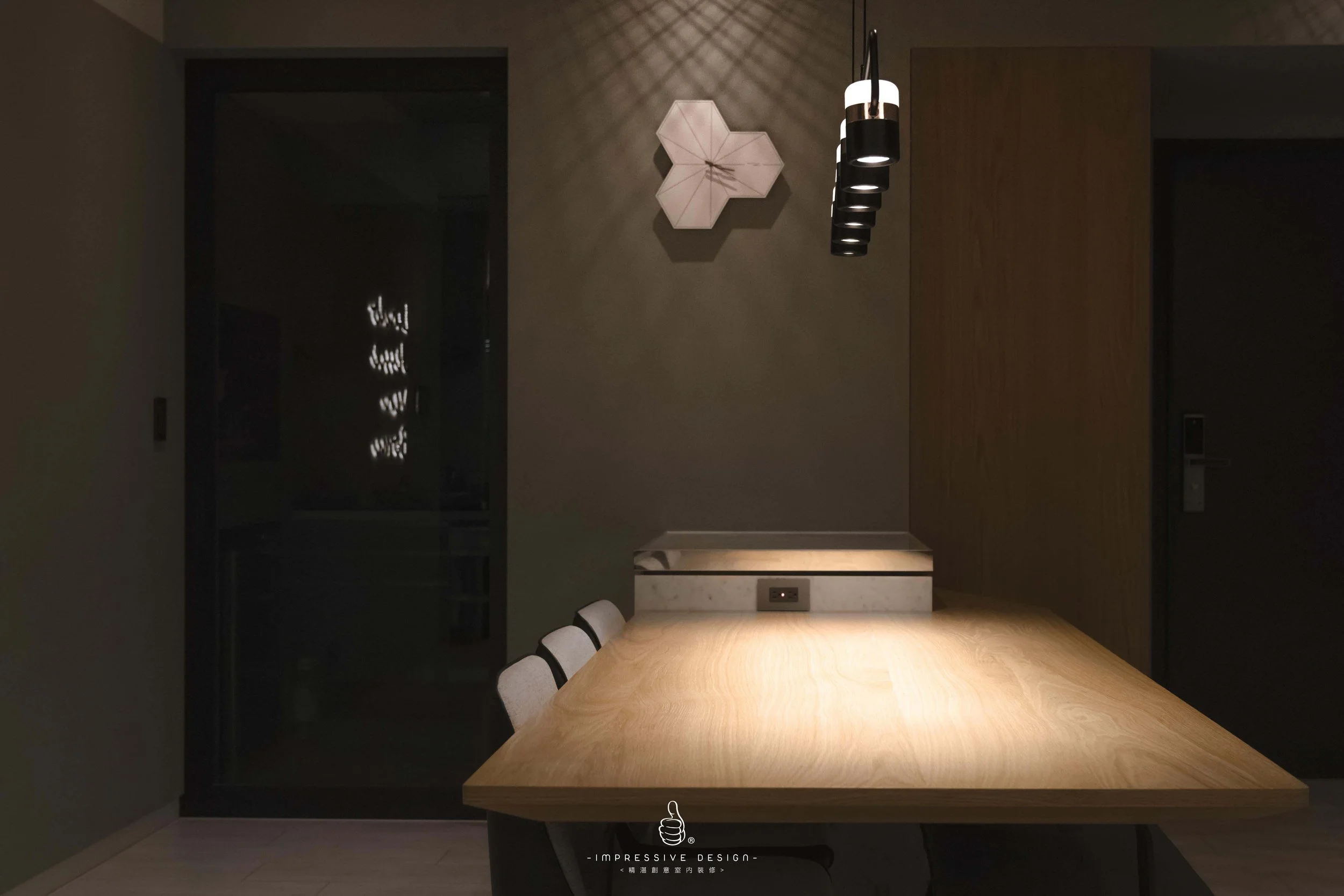 A minimalist dining room with a wooden table, three white chairs, a modern black pendant light, a decorative wall clock, and a built-in small alcove with lighting.